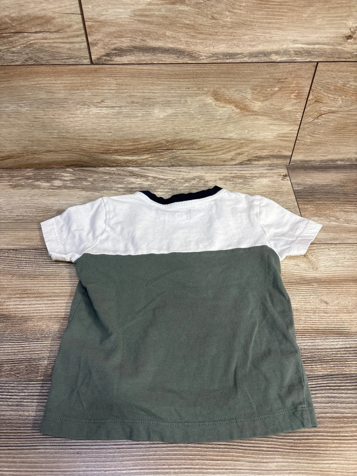 Rear view of toddler green and white colorblock short-sleeve shirt showing navy ribbed collar on wood floor background