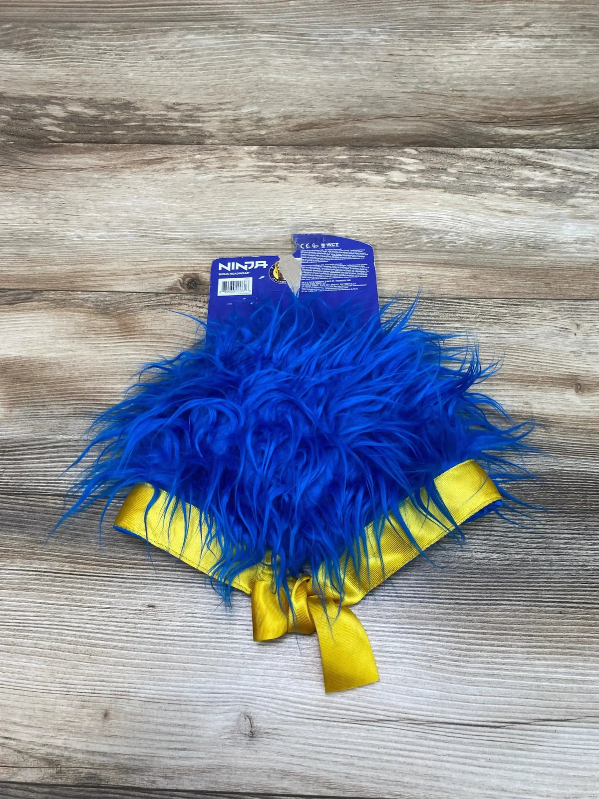 Top view of Ninja blue hair headgear showcasing shaggy blue strands and a yellow tie band on a wood surface