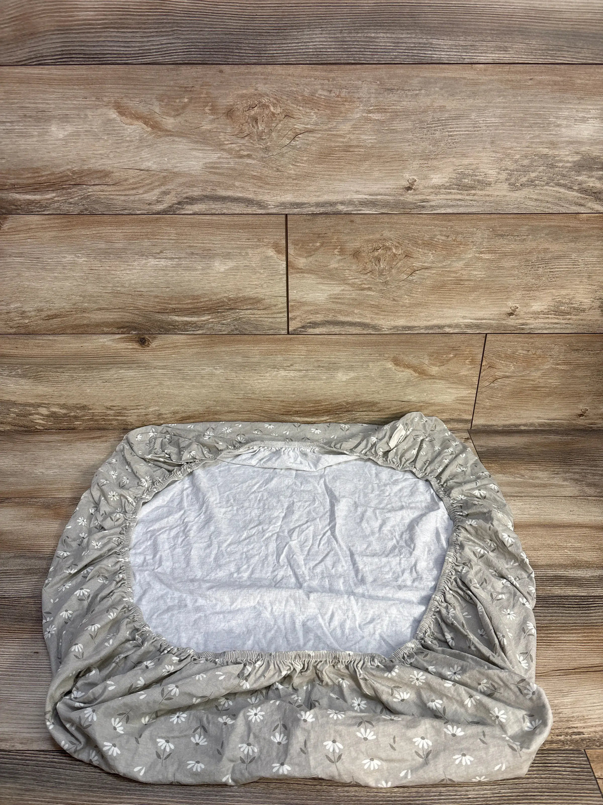 Top view of KeaBabies Soothe fitted mini crib sheet showcasing elasticated corners and floral beige fabric on wood flooring