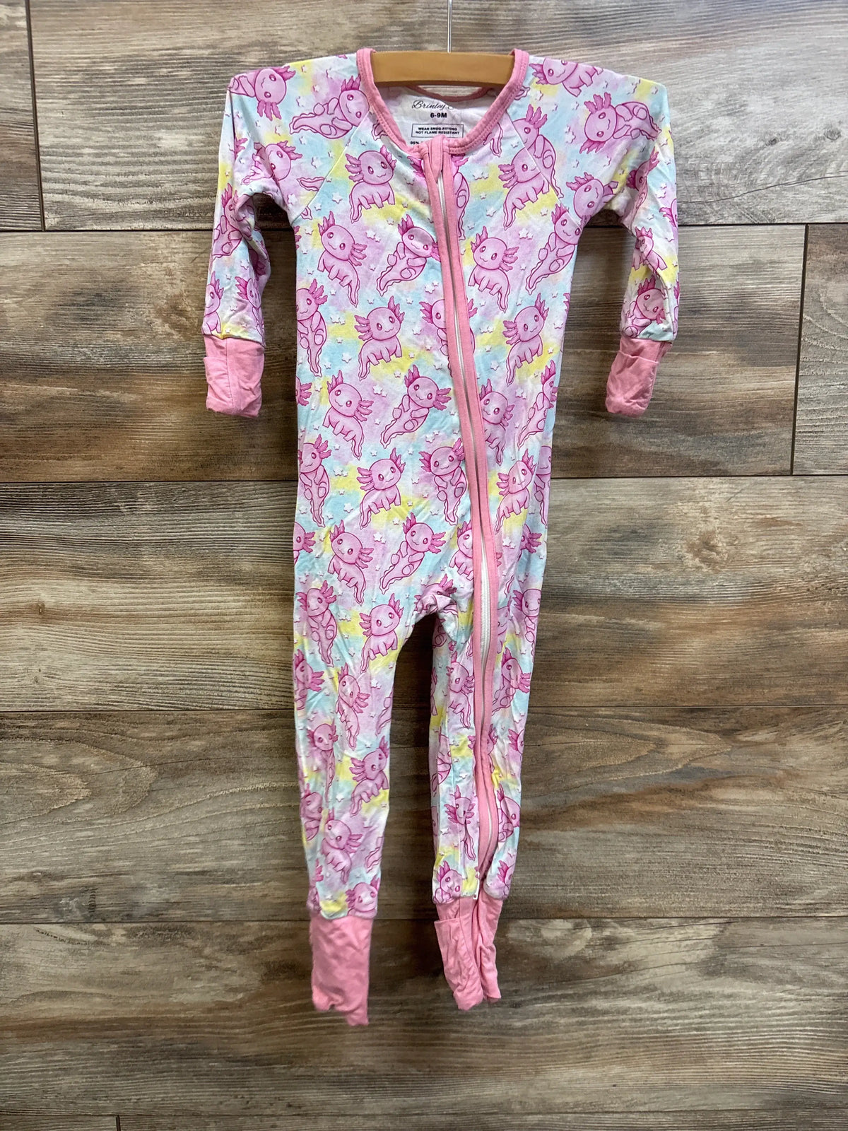 Front view of Brinley Jo pink bamboo convertible footie showcasing unicorn print and full-length zipper on wood flooring