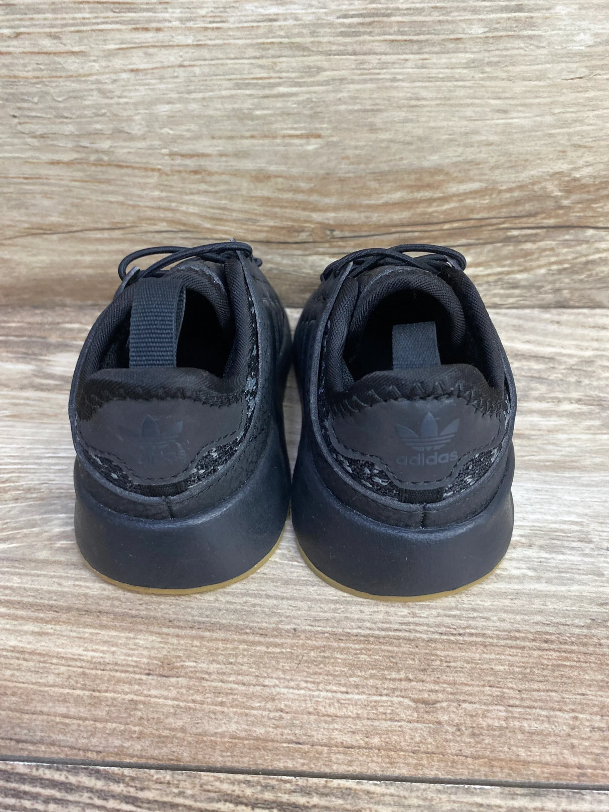 Black Adidas toddler sneakers, back view, on wood floor, gently used kids shoes