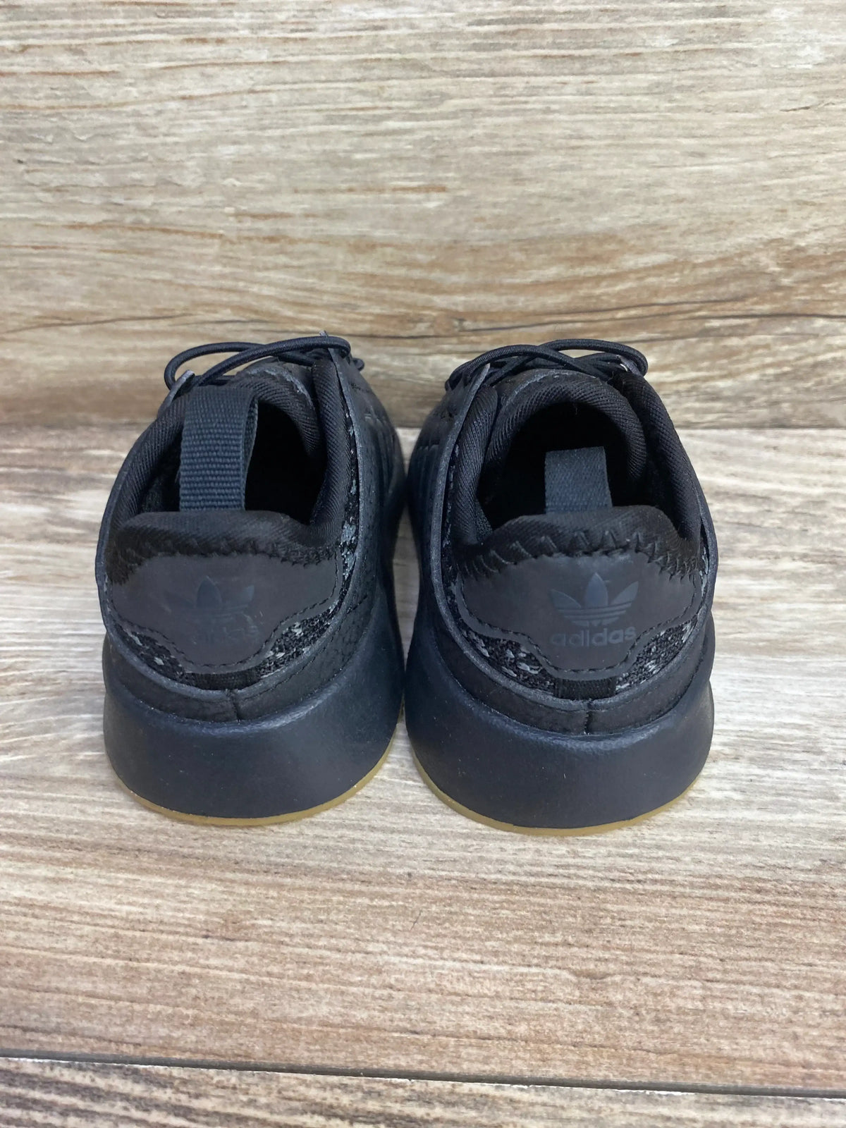 Black Adidas toddler sneakers, back view, on wood floor, gently used kids shoes