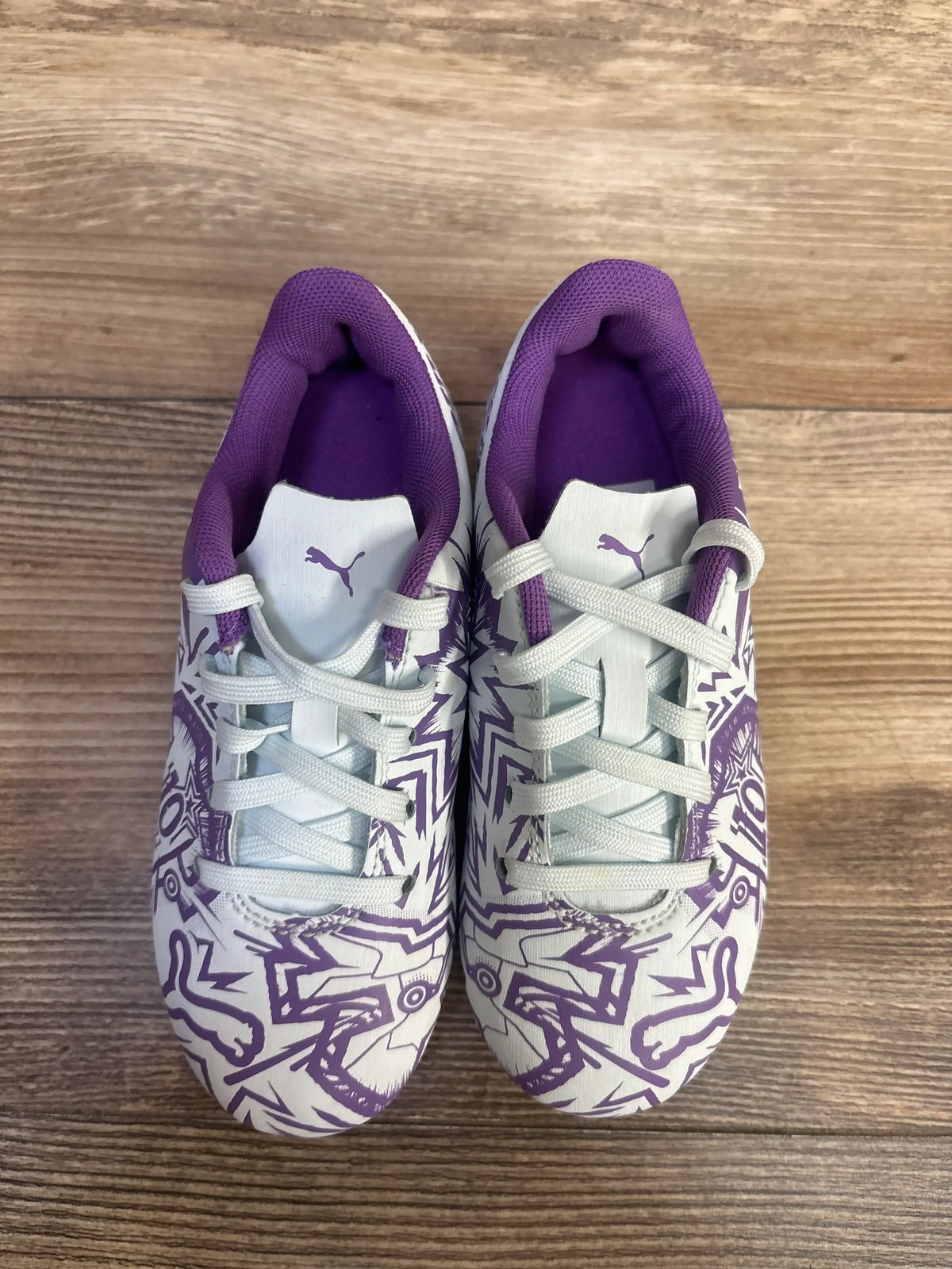 Top view of Puma Tacto II soccer cleats showcasing white laces and purple graphic uppers on a wood floor