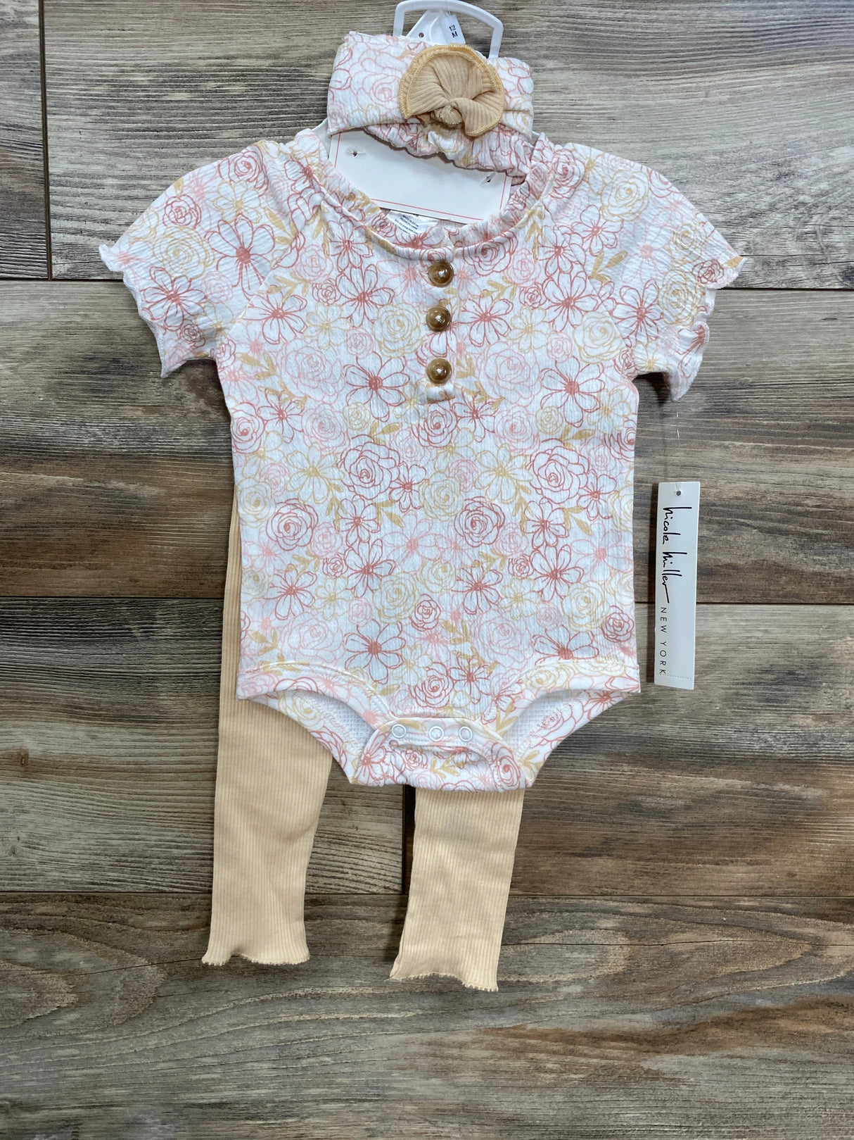 Floral baby bodysuit with buttons, beige ribbed leggings, and matching headband on wooden floor