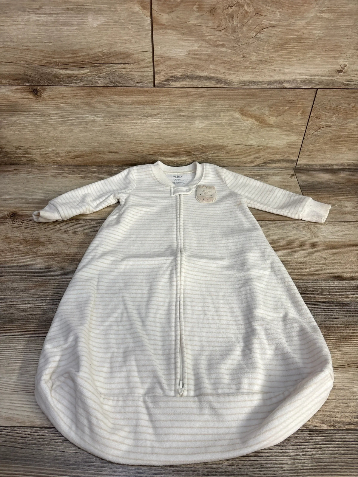 Front view of Carter’s ivory blanket sleep sack for 0-3 months, with front zipper and enclosed bottom on wood