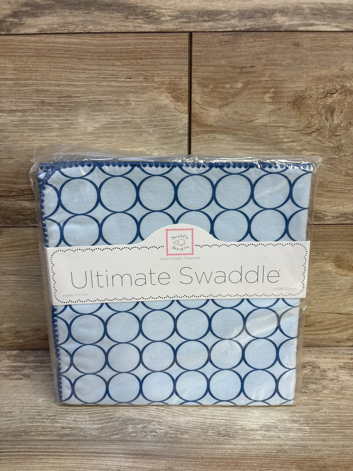Blue circle pattern cotton swaddle blanket in packaging, baby essentials product on wood background