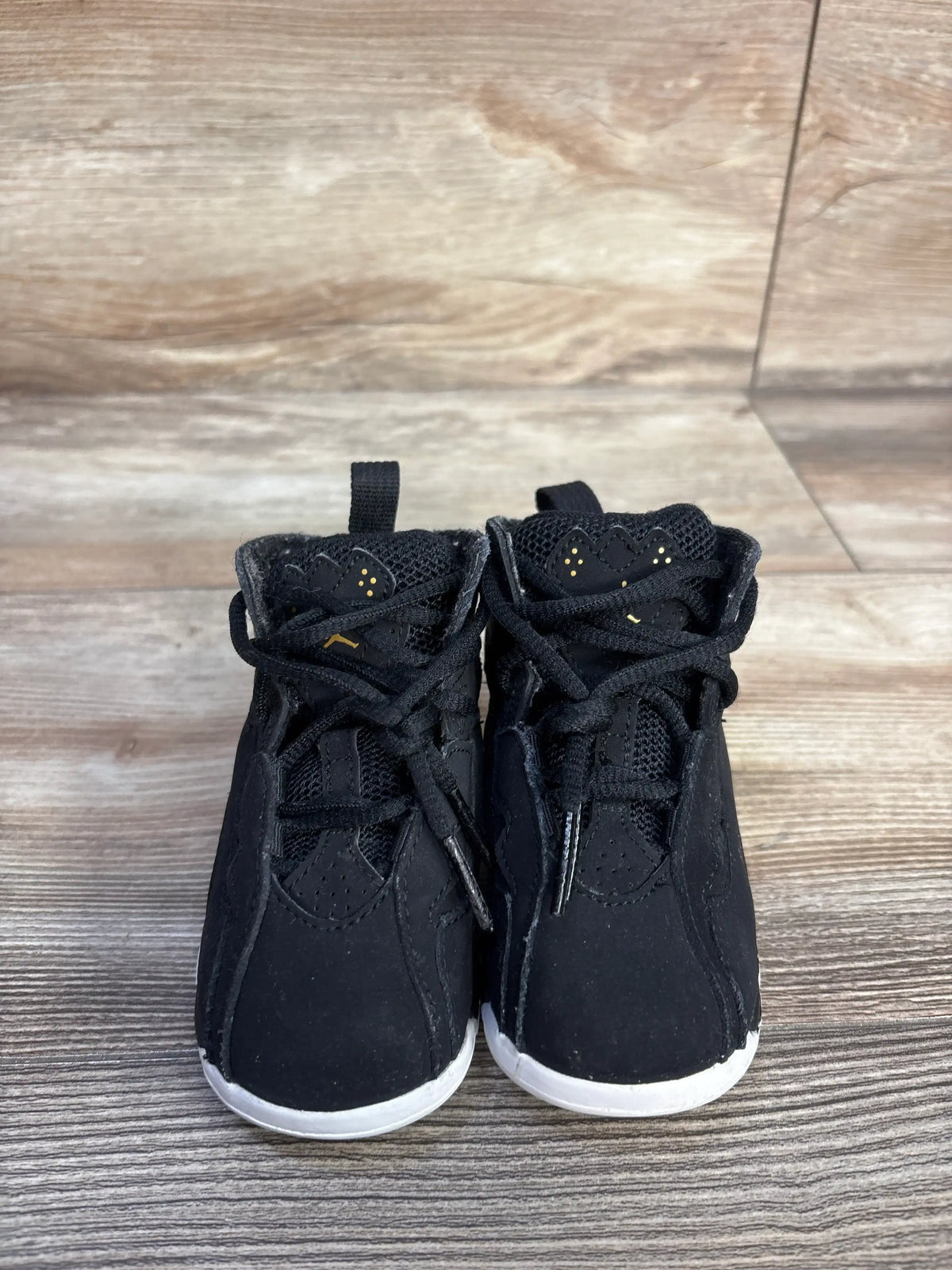 Front view of Air Jordan True Flight BT black sneakers showcasing gold Jumpman logos and white rubber outsoles on a wood floor