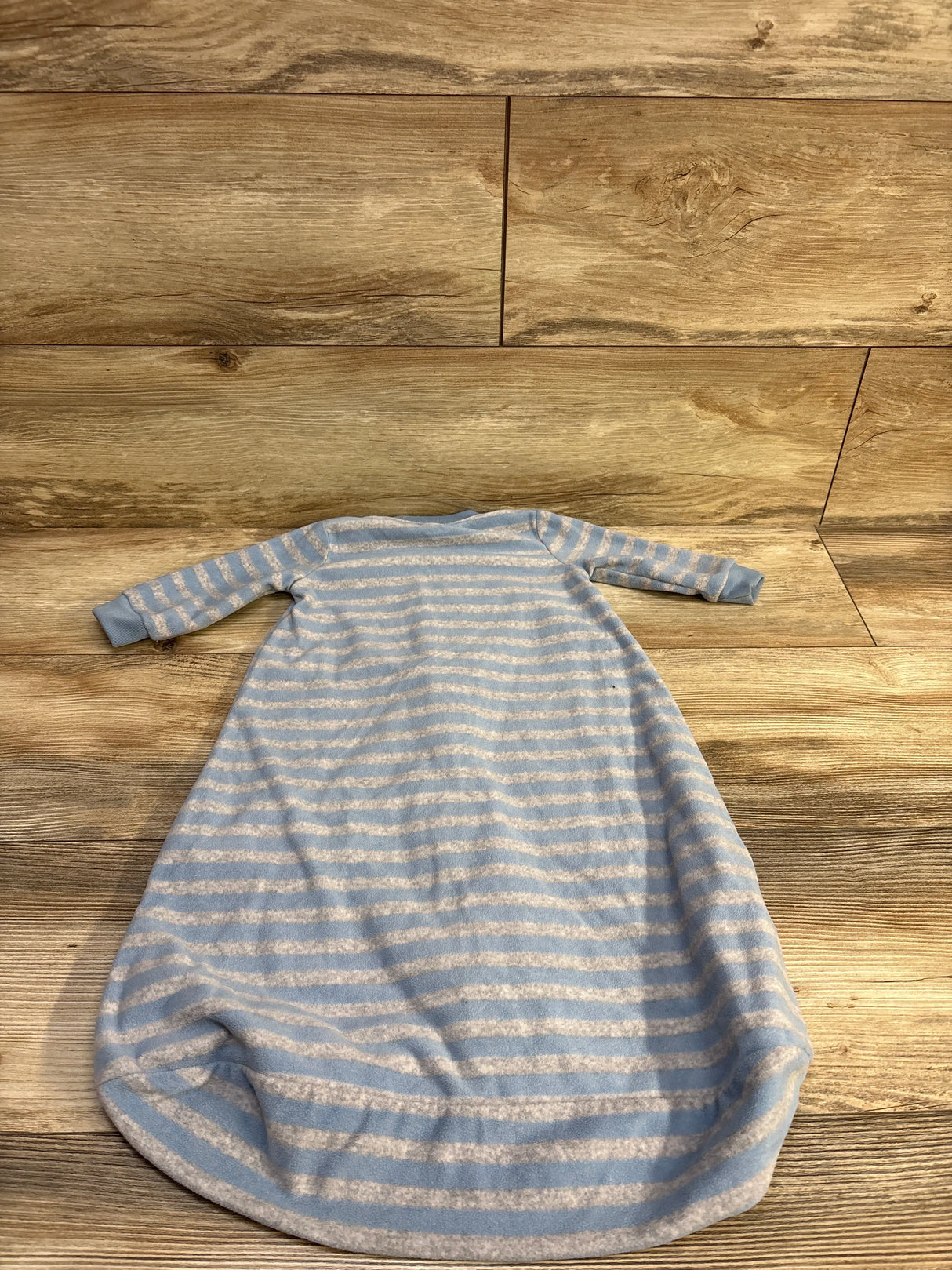 Flat lay of Carter’s striped blue blanket sleep sack showcasing long sleeves and gathered bottom on wood floor background