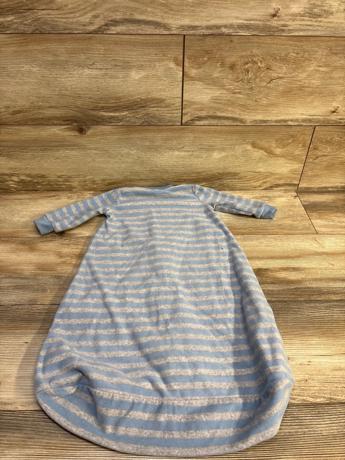 Flat lay of Carter’s striped blue blanket sleep sack showcasing long sleeves and gathered bottom on wood floor background