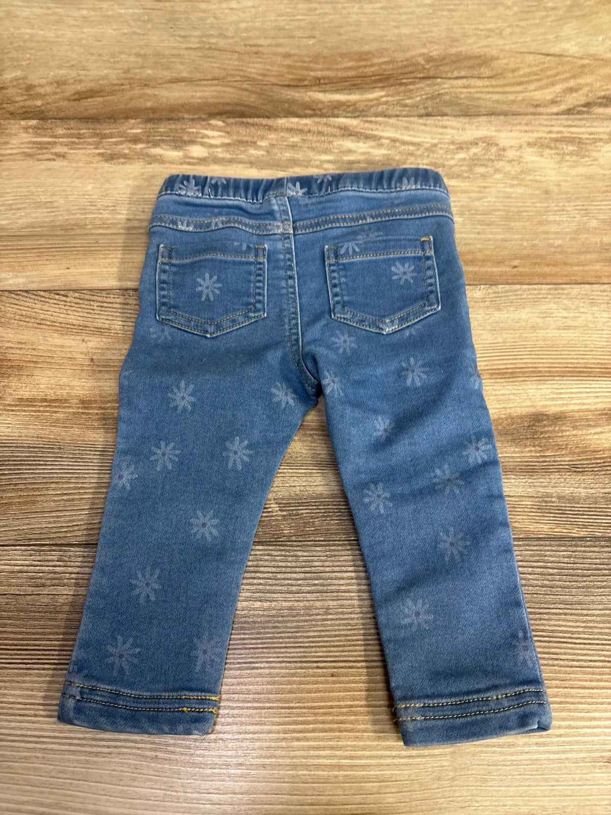 Back view of toddler blue denim jeans with elastic waistband and subtle flower patterns on wooden surface