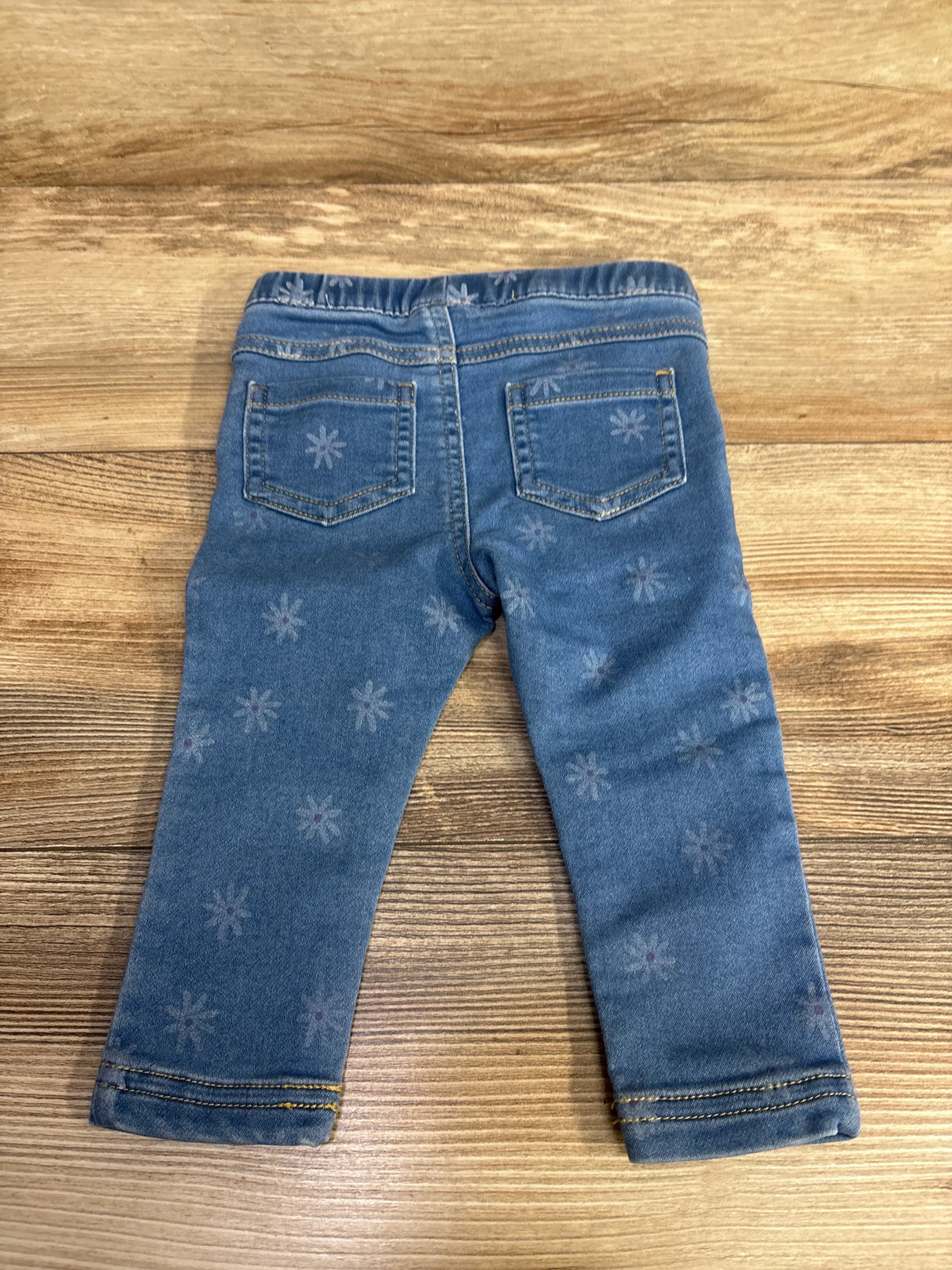 Back view of toddler blue denim jeans with elastic waistband and subtle flower patterns on wooden surface
