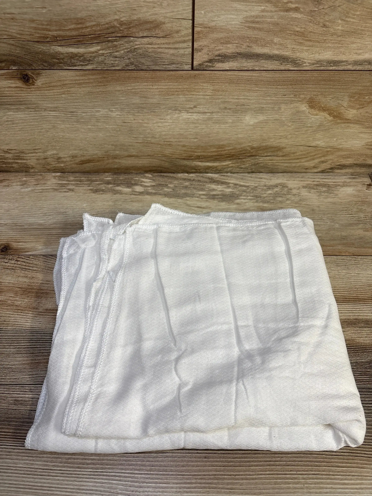 Top-down view of five folded white receiving blankets showcasing textured weave and overlocked edges with wood plank background