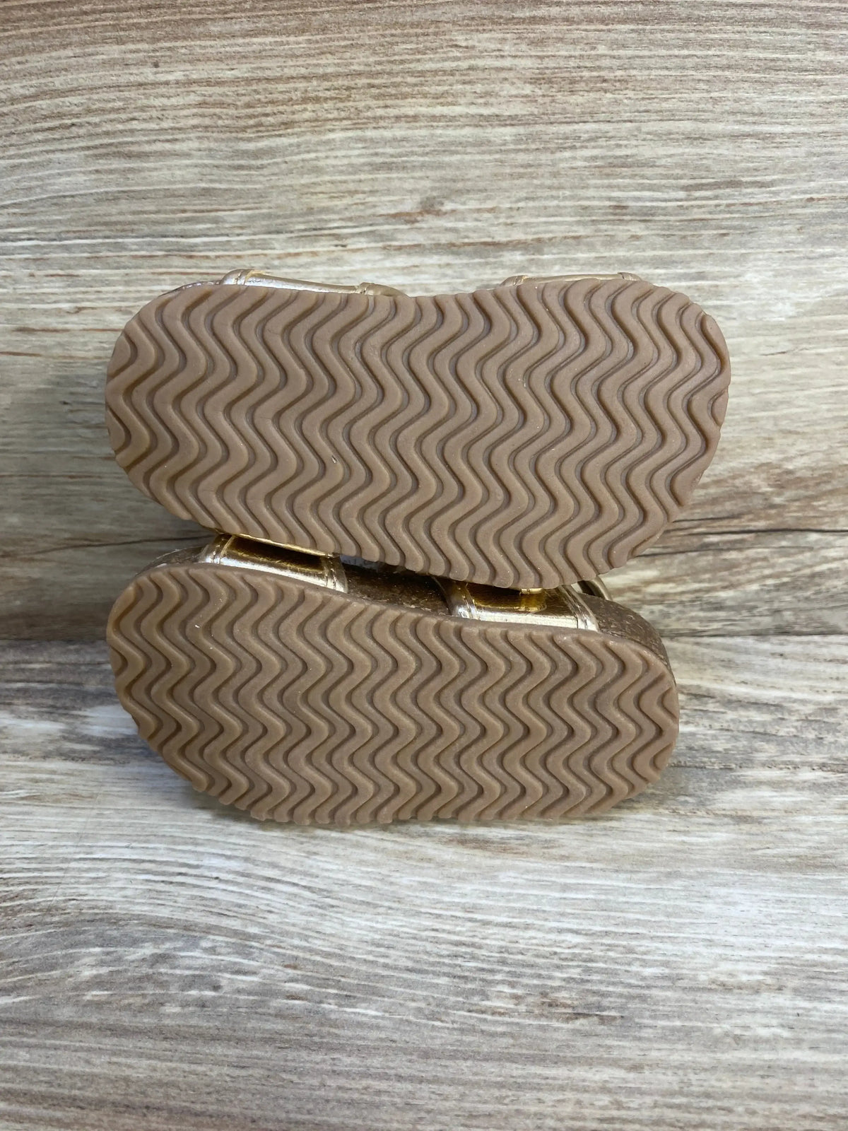 Bottom view of Just One You first-walker toddler sandals showcasing wavy rubber tread soles on wooden background