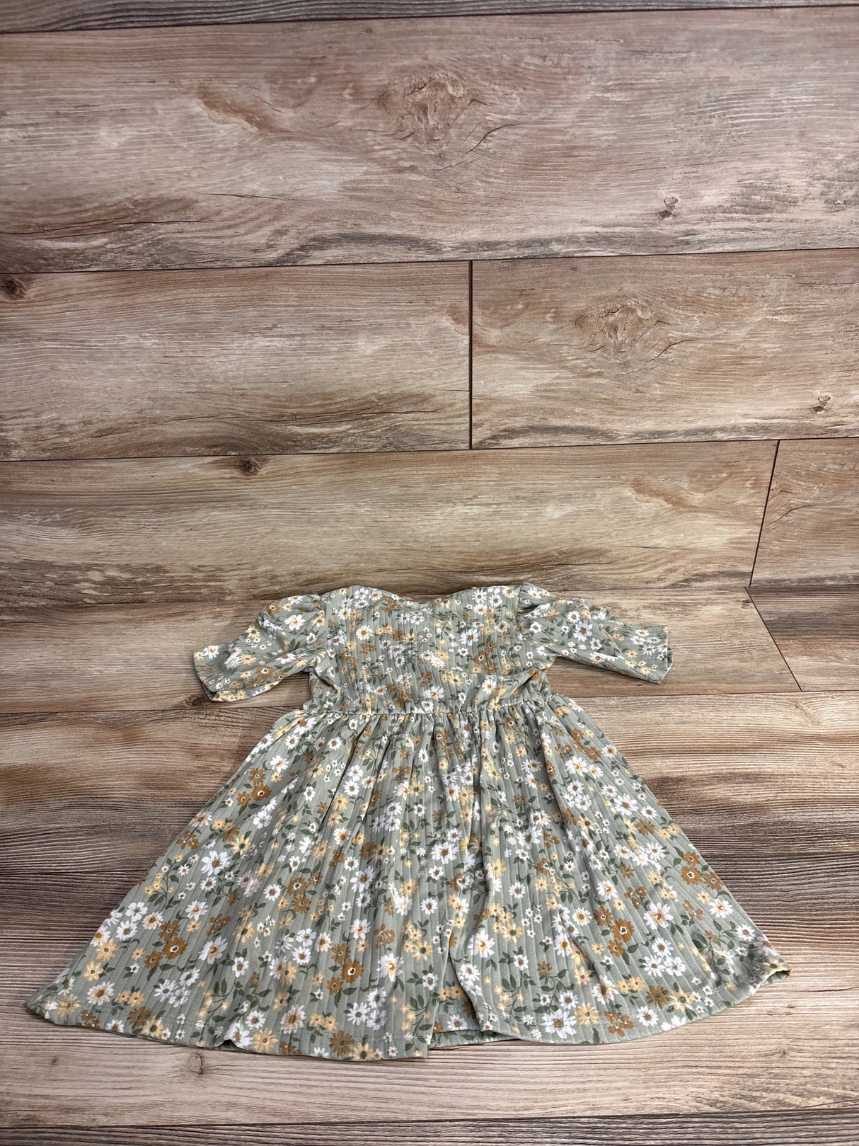 Green floral baby dress with white, yellow, and orange flowers on wood background