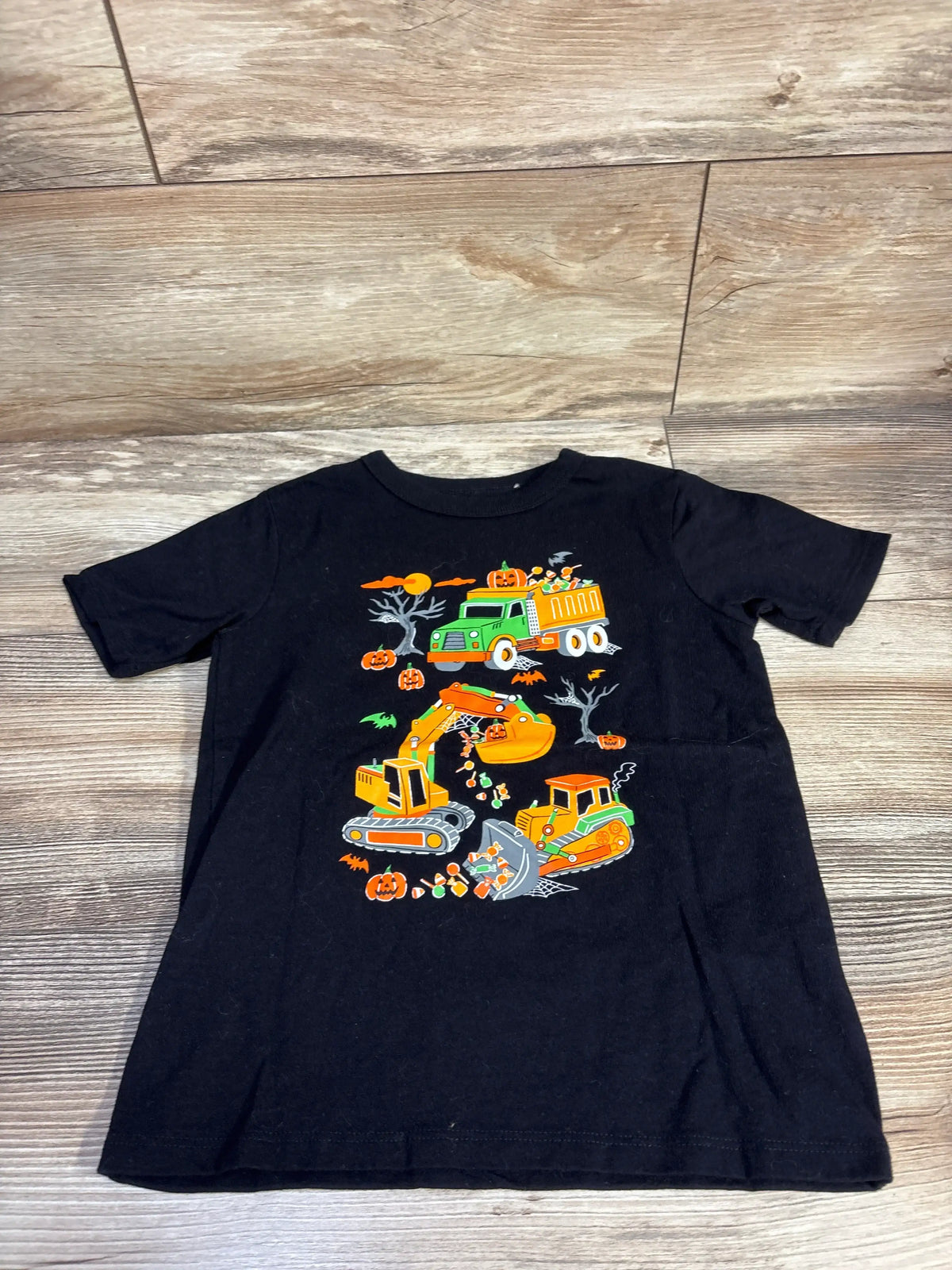 Front view of Children’s Place Halloween vehicle shirt showcasing colorful construction graphics on black fabric over a wood floor