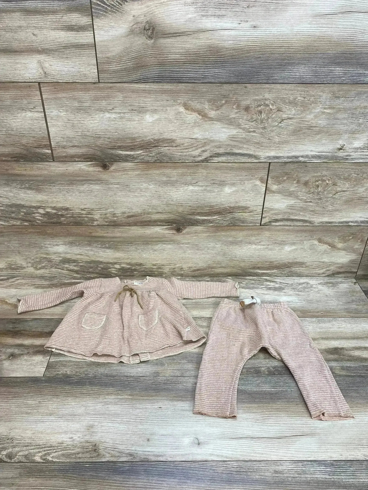 Flat lay of baby blush-striped ribbed blouse and matching pants set, size 6M, showing front pockets and elastic waist with bow on wood floor background