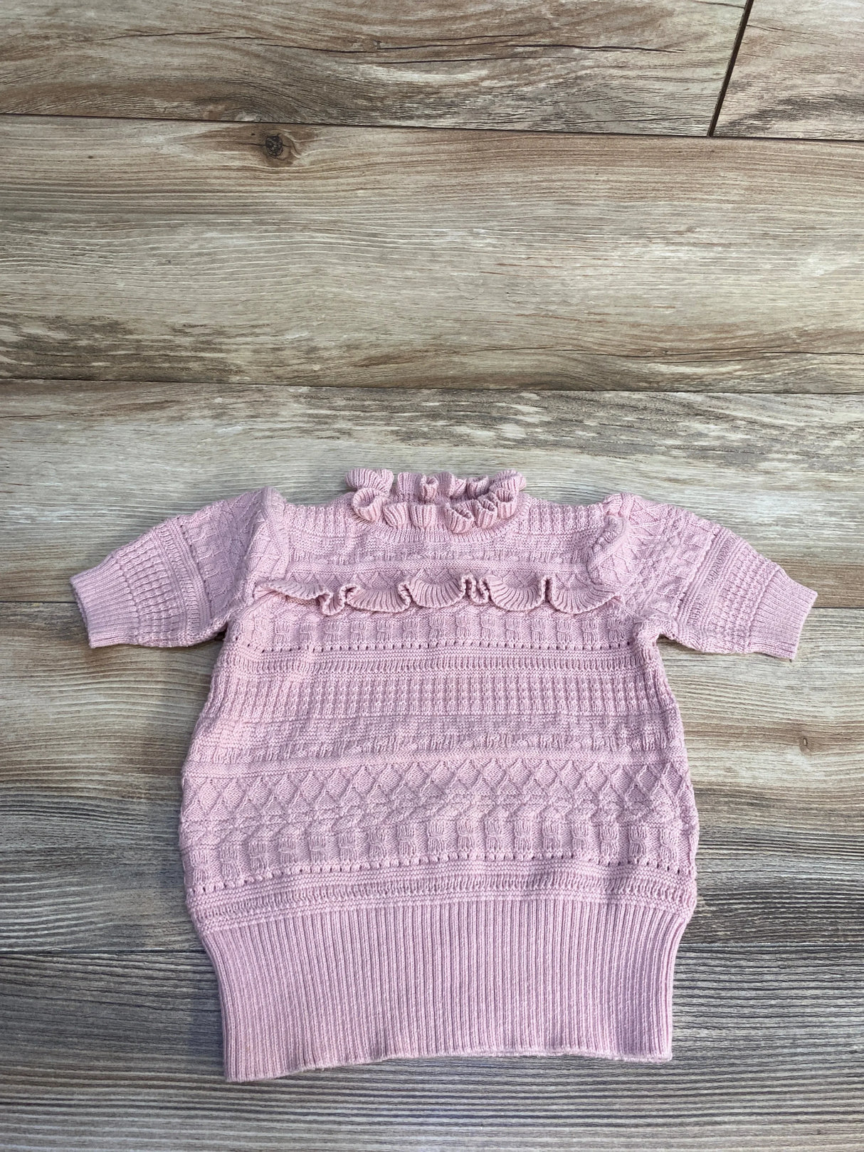 Flat lay of peach Janie and Jack baby sweater top showing ruffled collar and textured cable knit pattern on wood backdrop