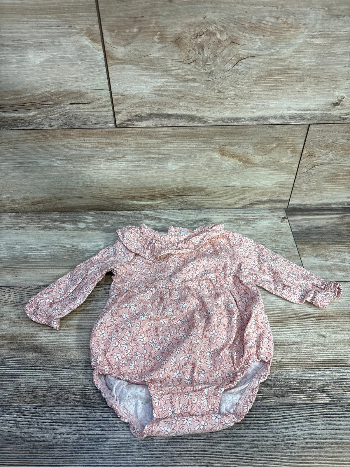 Top view of Just One You pink floral bubble romper with long sleeves, ruffled collar, and bubble hem on wood-look floor