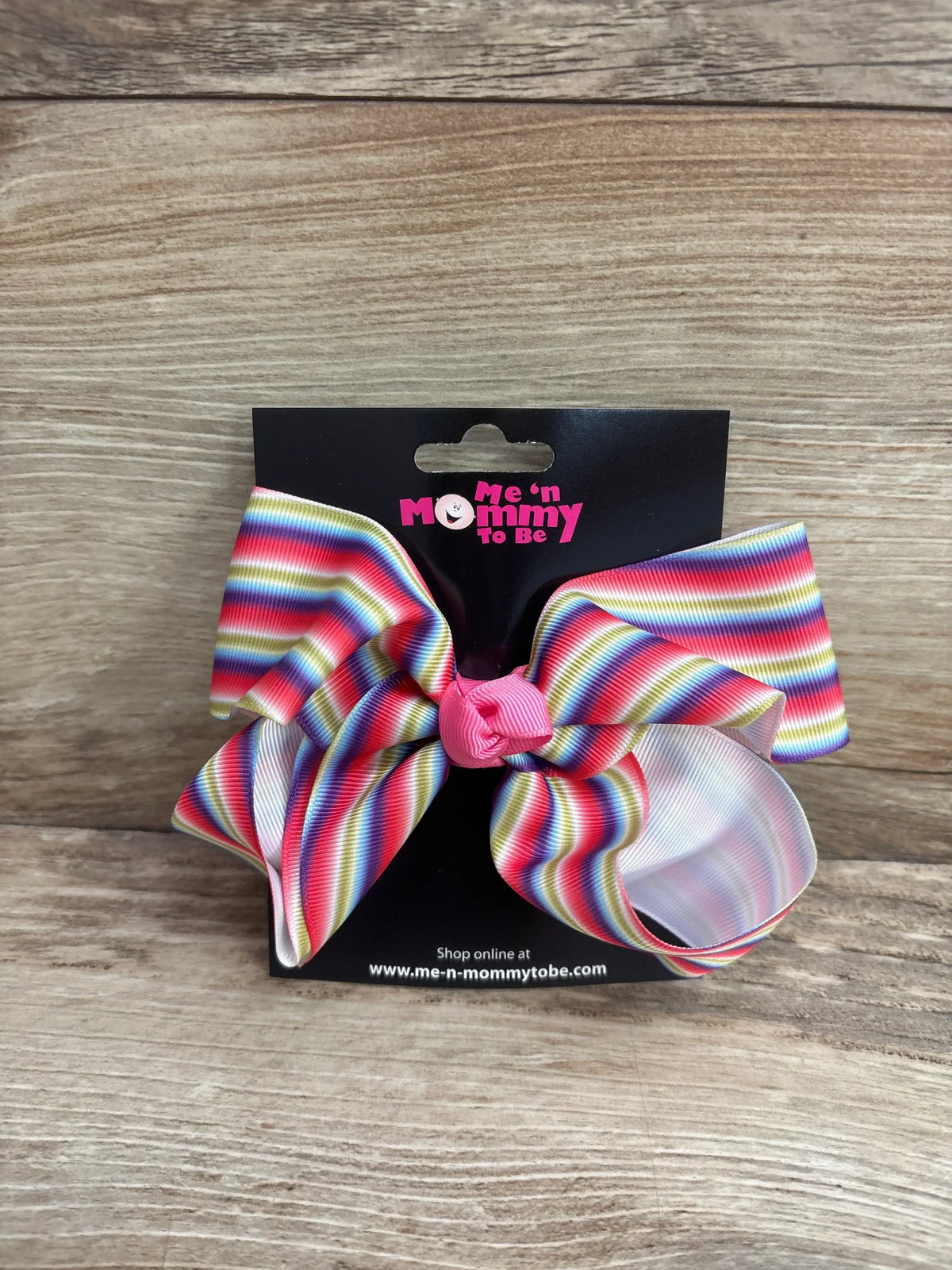 Front view of large striped rainbow hair bow with pink center knot on black Me n Mommy To Be display card on wood background