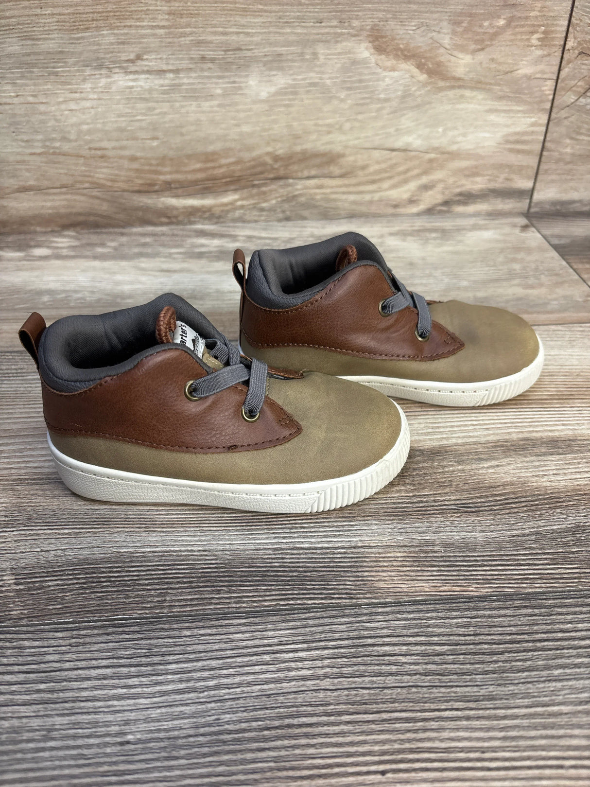 Brown and tan toddler sneakers with gray laces on wood background, gently used kids shoes