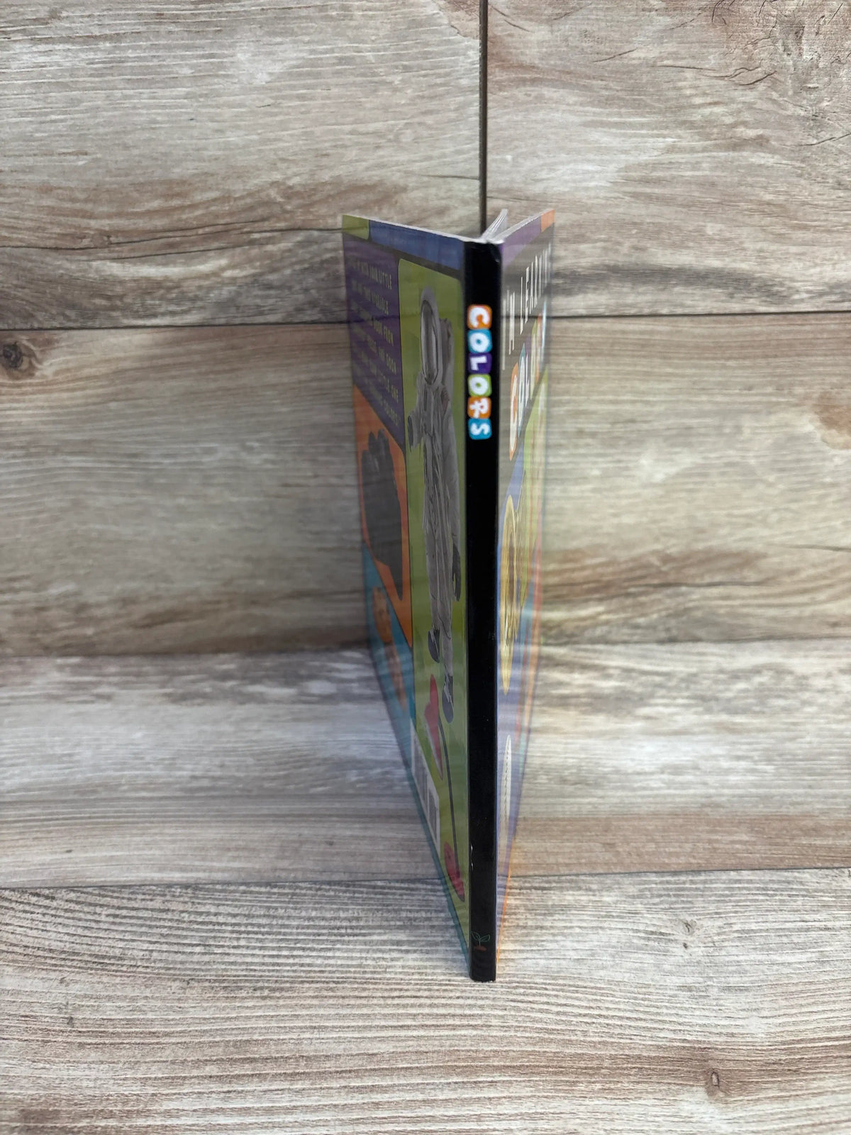 Angled view of I’m Learning Colors board book showing its colorful spine labeled COLORS and thick cover on a wood grain background