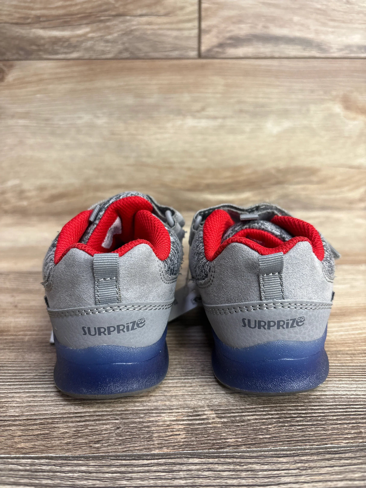 Rear view of children's Surprize brand grey sneakers with red inner lining and blue soles on wooden floor