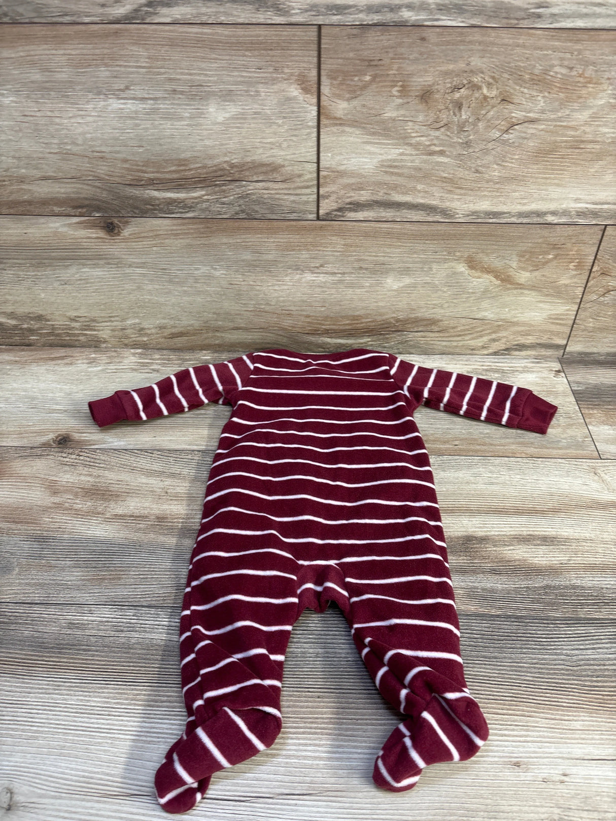 Flat lay of Carter’s maroon and white striped blanket sleeper with feet, size 3 months, on wood floor background