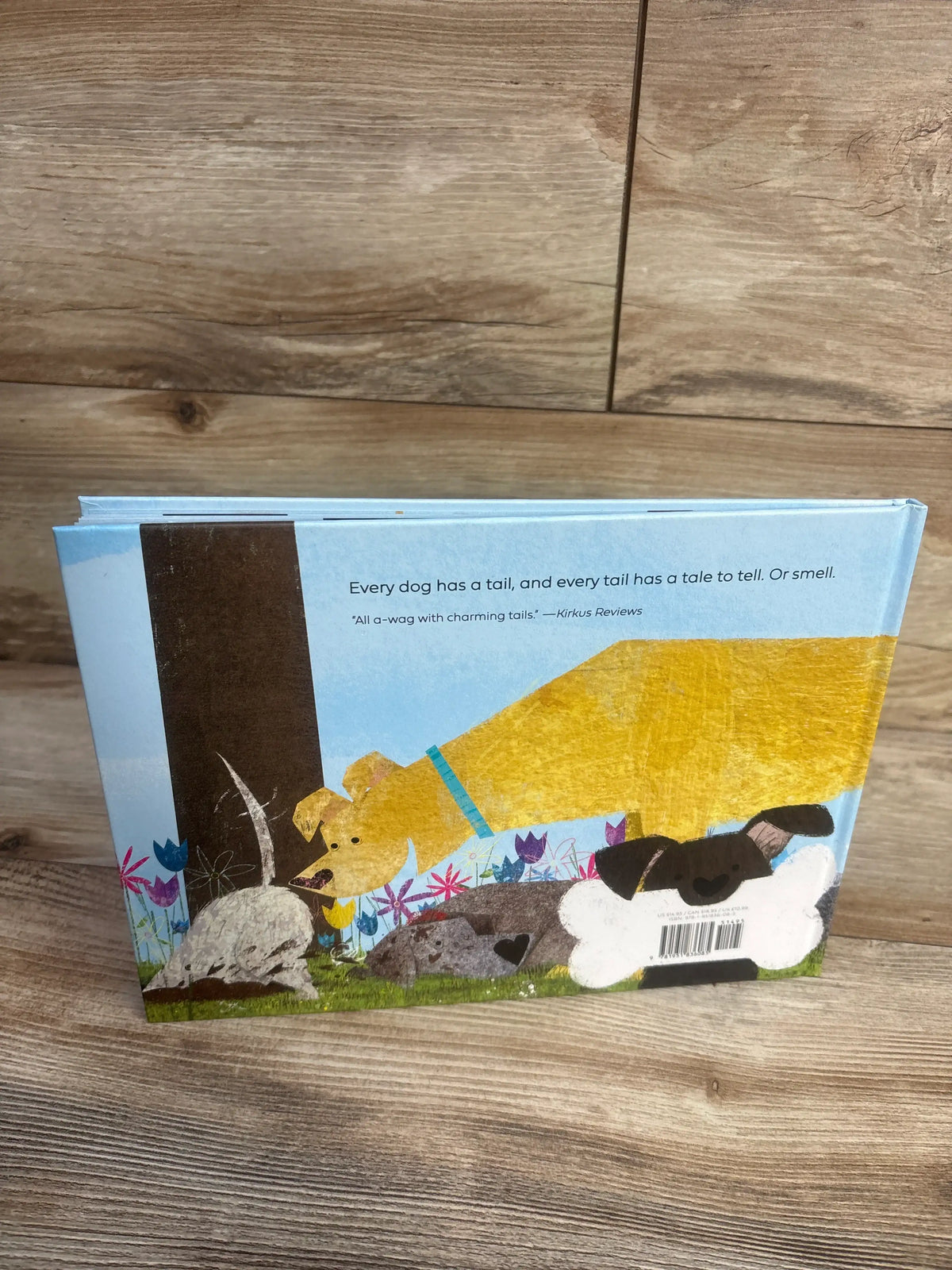 Back cover of Love Tails Hardcover Book showing illustrated dogs and tail-themed text on a wood floor