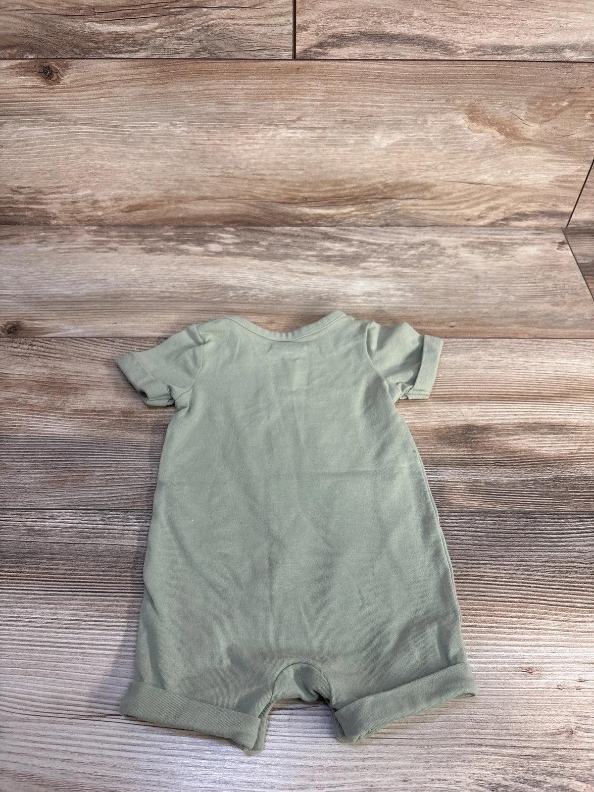 Back view of Cat and Jack green shortie romper in size zero to three months, showcasing short sleeves and cuffed legs on a wood-look background
