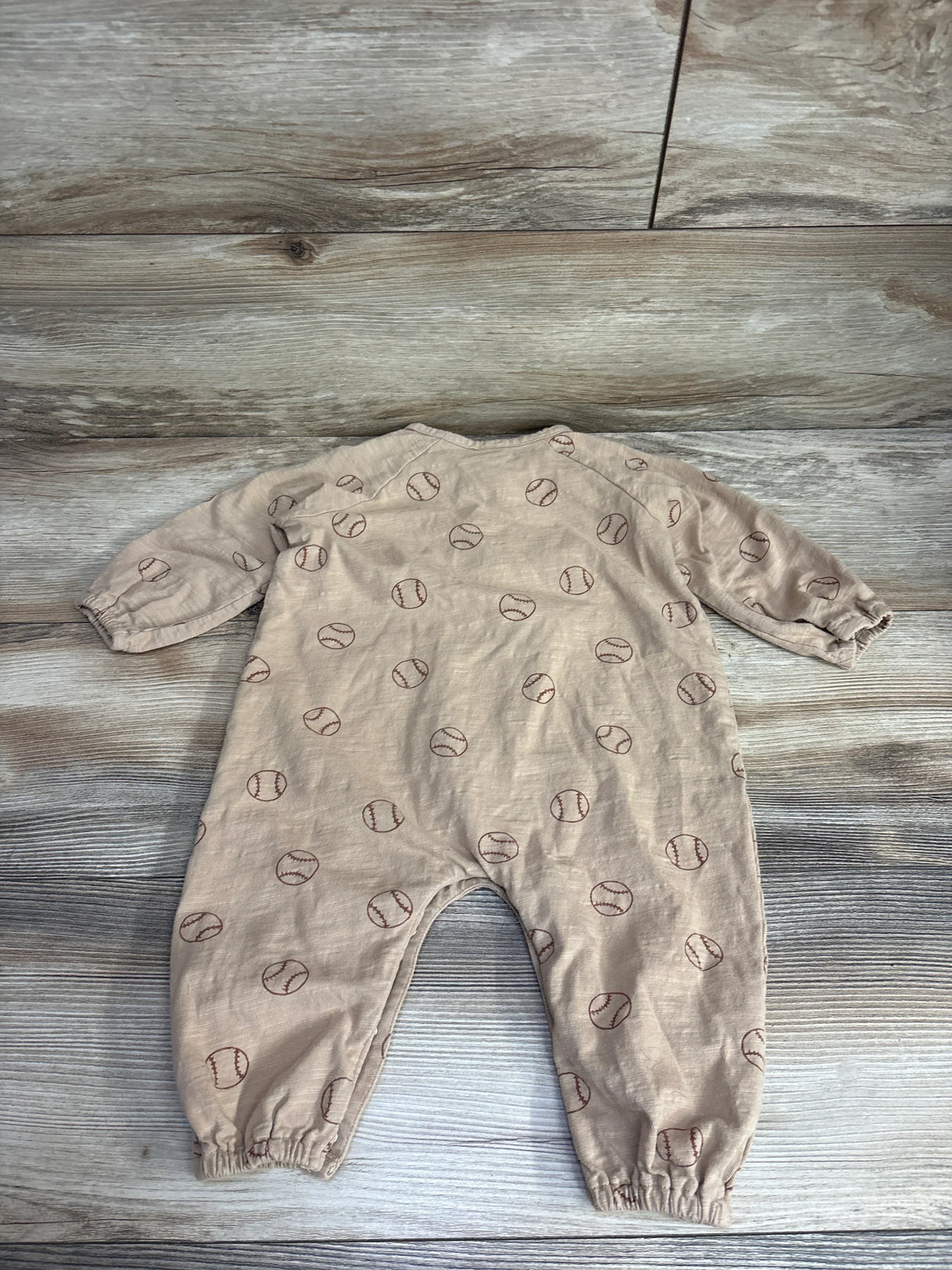 Beige baby romper with brown baseball print on wooden floor from kids resale store