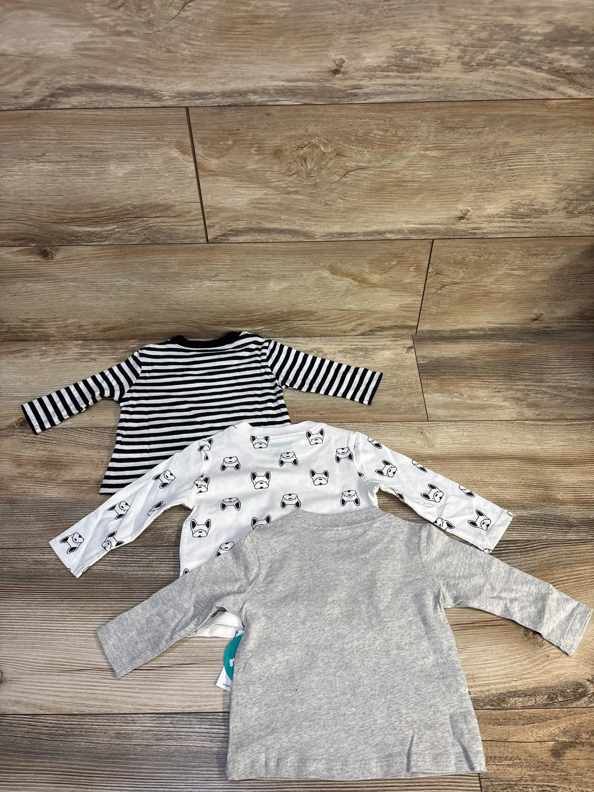 Top view of Mighty Goods three pack long sleeve shirts showcasing stripes, dog prints, and gray fabric on wood flooring