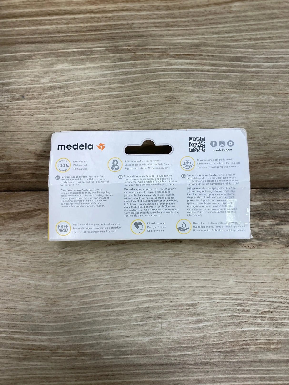Back view of Medela Purelan lanolin nipple cream 1.3 oz box showing information, icons, and Medela logo on wood surface