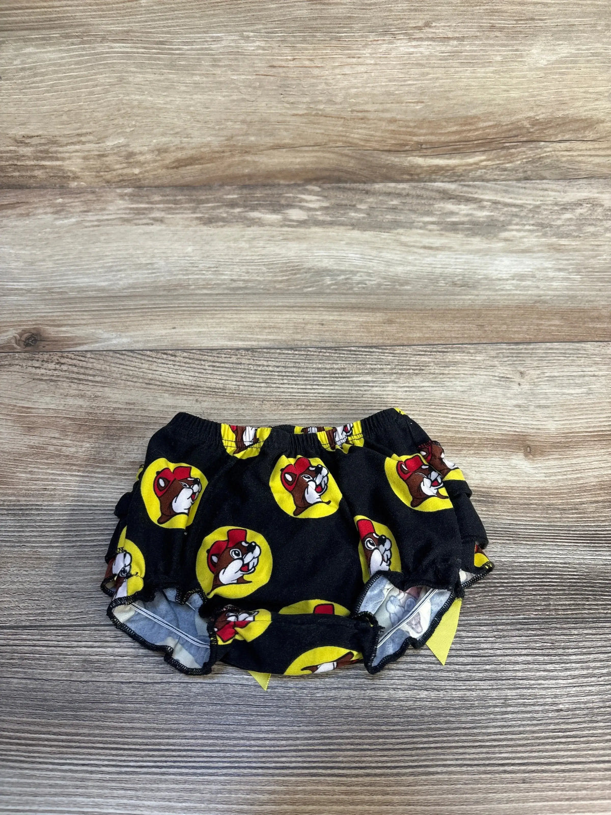Black baby bloomers with cartoon dog face print and yellow circles on wood background