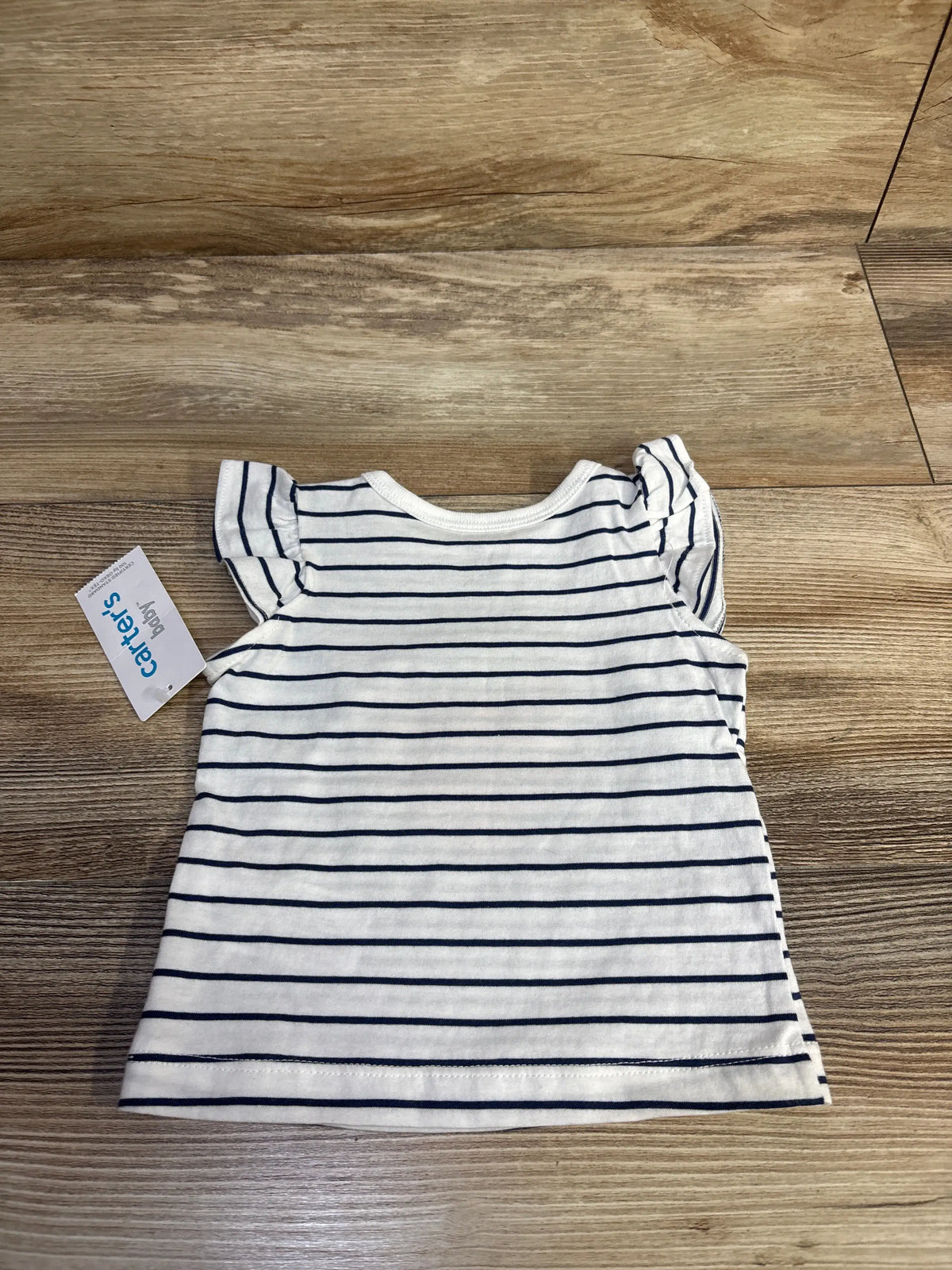 Front view of white baby shirt with navy horizontal stripes and ruffled cap sleeves on wood background