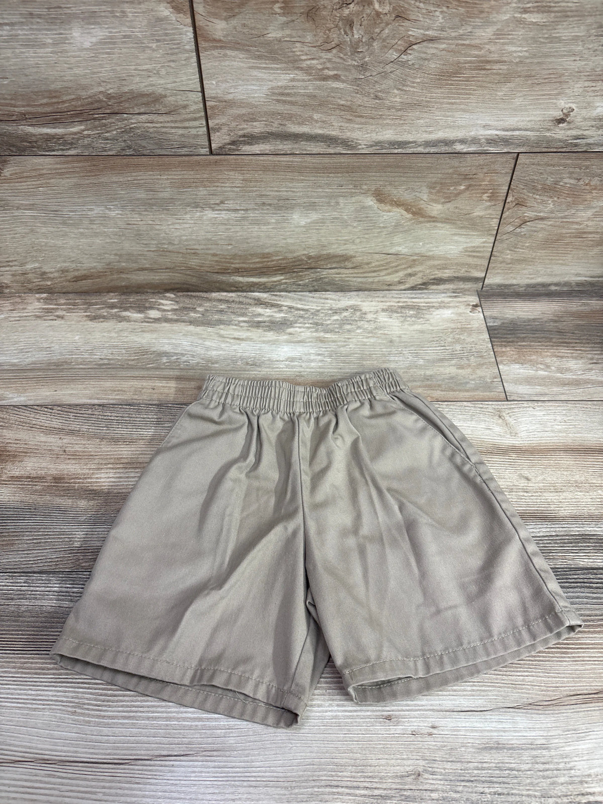 Classroom brand tan uniform shorts for kids size 5T on a wood background