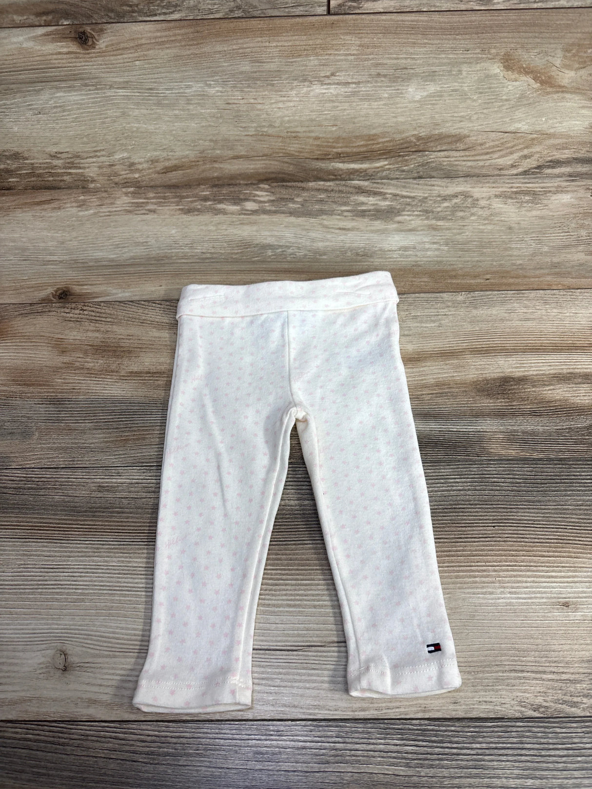 White baby leggings with subtle pink polka dots and a small logo on the ankle, laid flat on wood