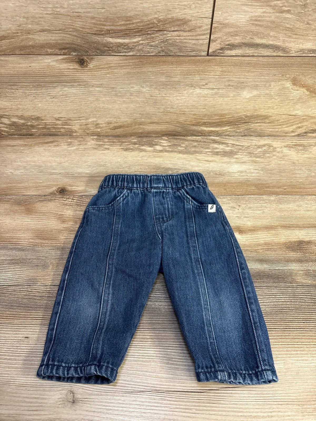Flat lay of navy pull-on baby jeans (12 months) with elastic waistband, faux pockets and center seam details on wood background