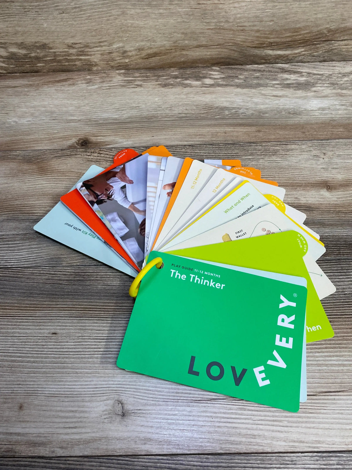 Lovevery play guide cards for 11-12 months titled The Thinker fanned out on a wood surface