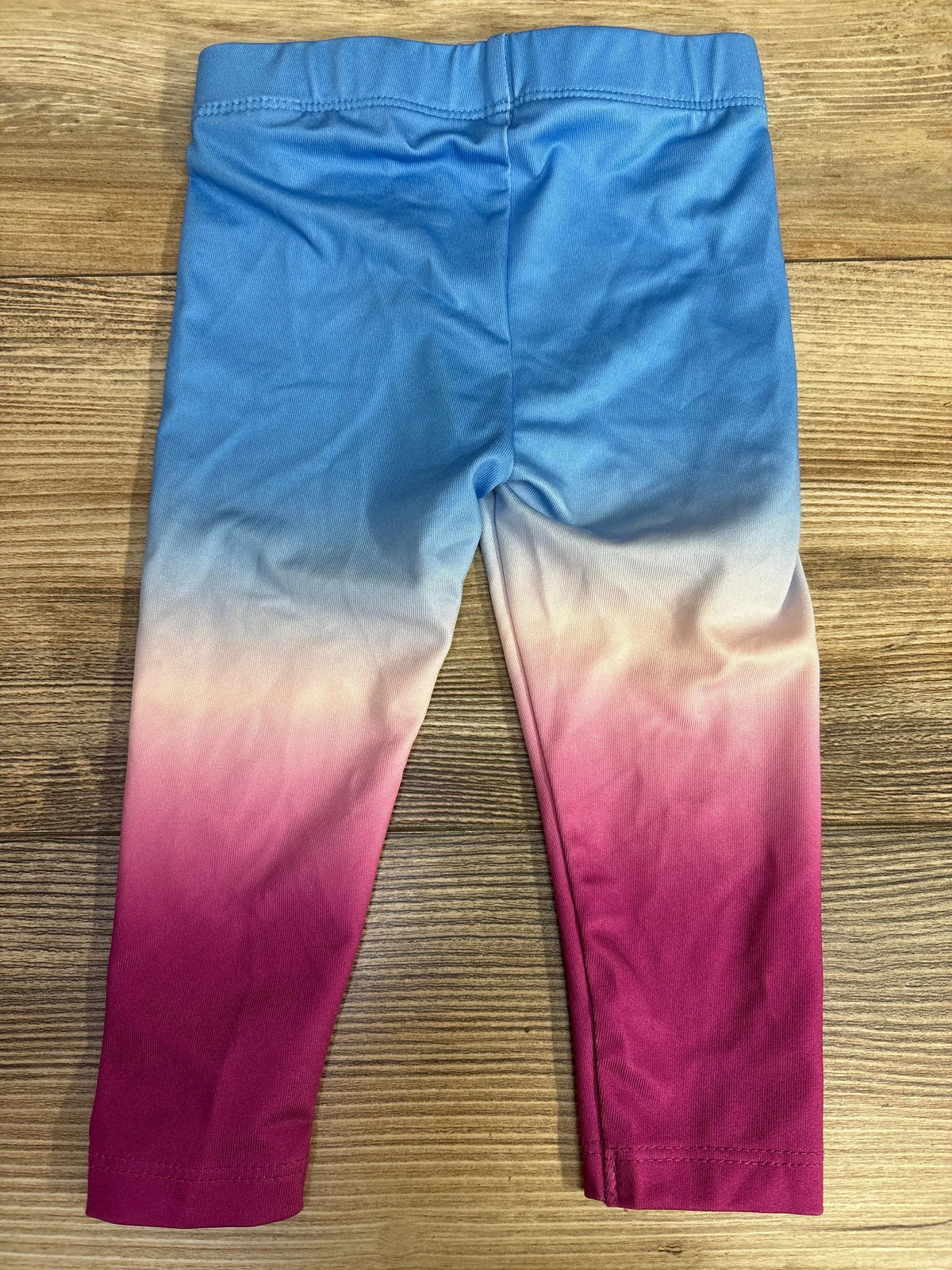 Children's ombre leggings with blue, white, and pink gradient on wood background