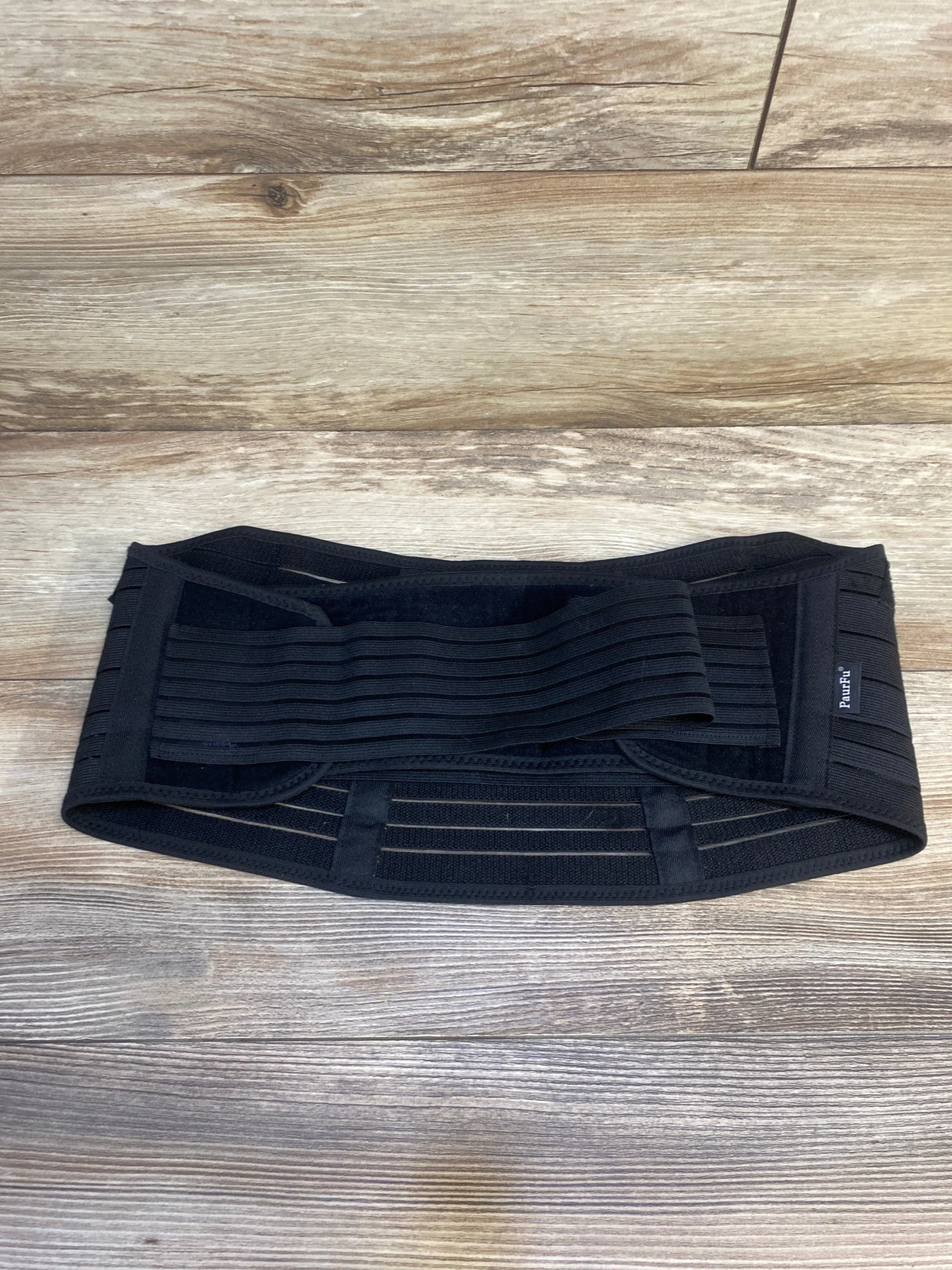 Black adjustable maternity support belt on wood floor, postpartum belly band