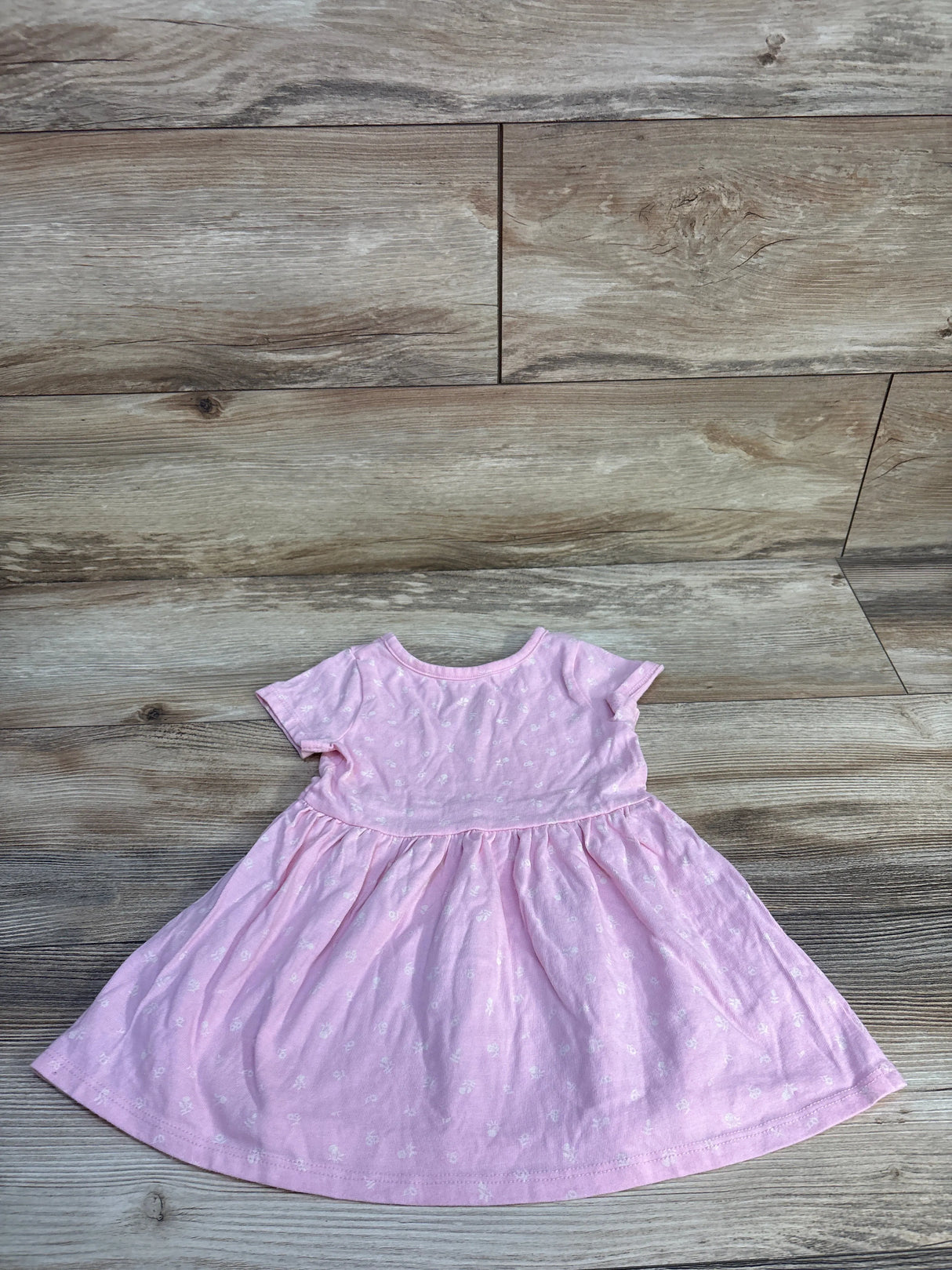Flat lay of pink toddler dress 18 months showing short sleeves, gathered skirt and small white floral print on wood floor