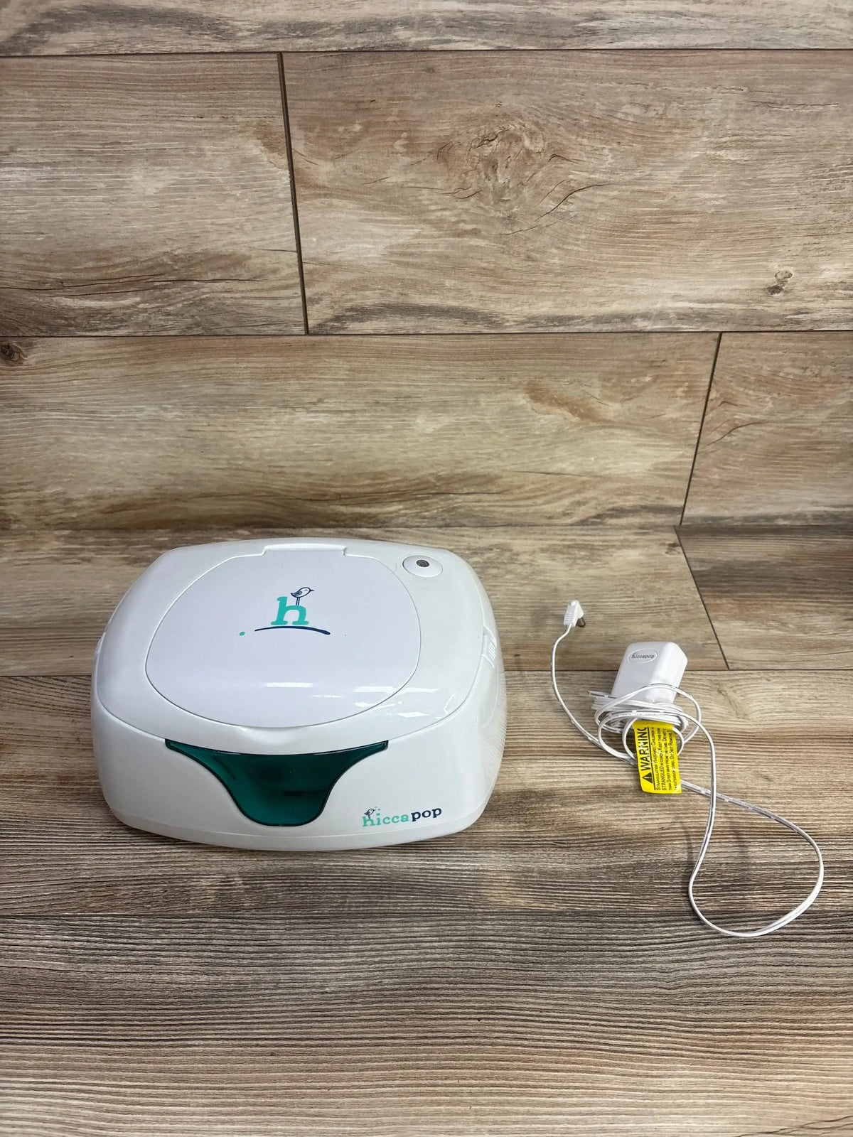 Hiccaclean baby wipe warmer with white and teal design and power adapter on wooden surface