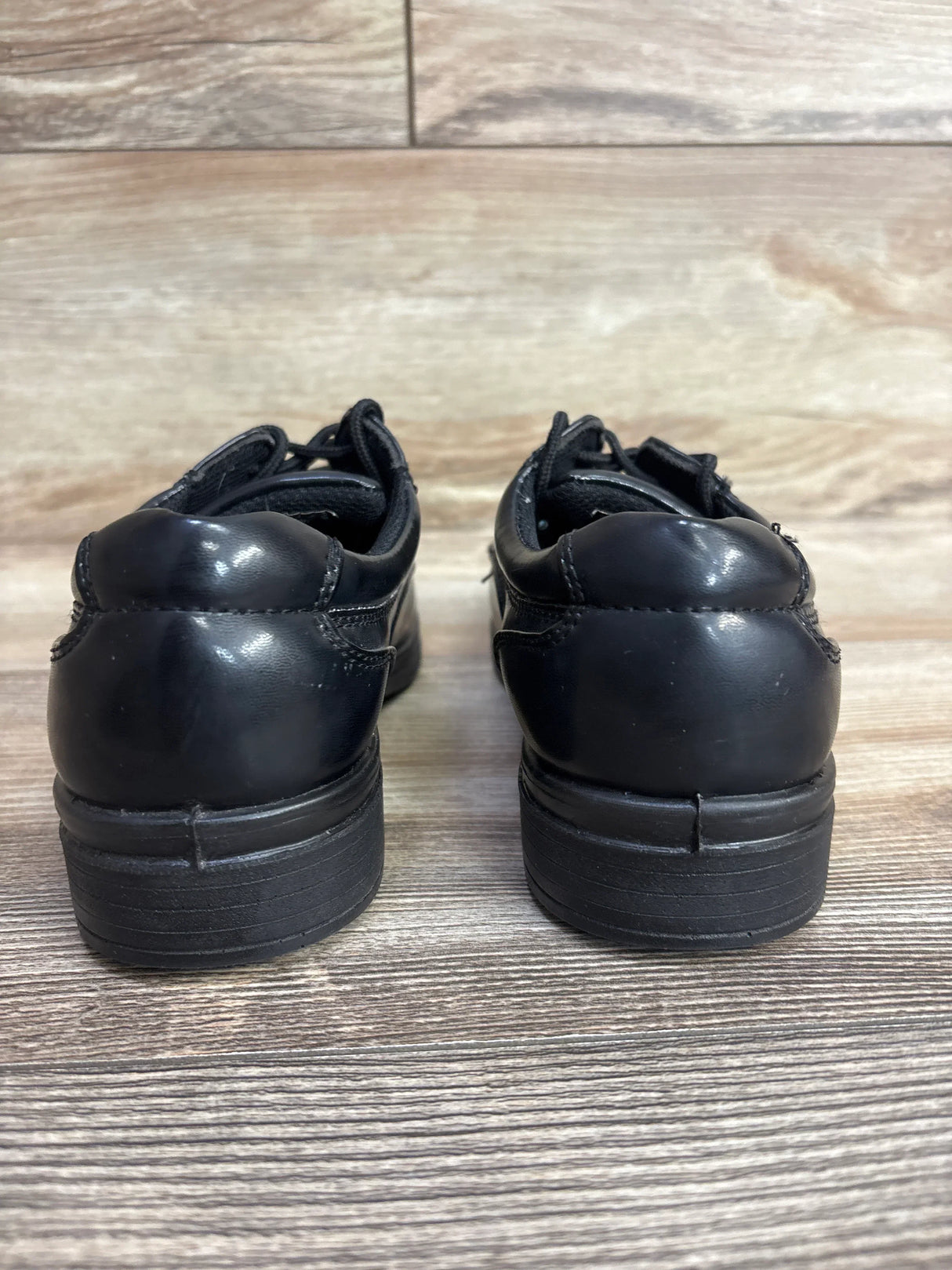 Rear view of black Deer Stags Sharp dress shoes, size 2Y, showcasing padded collars and traction soles on a wooden floor