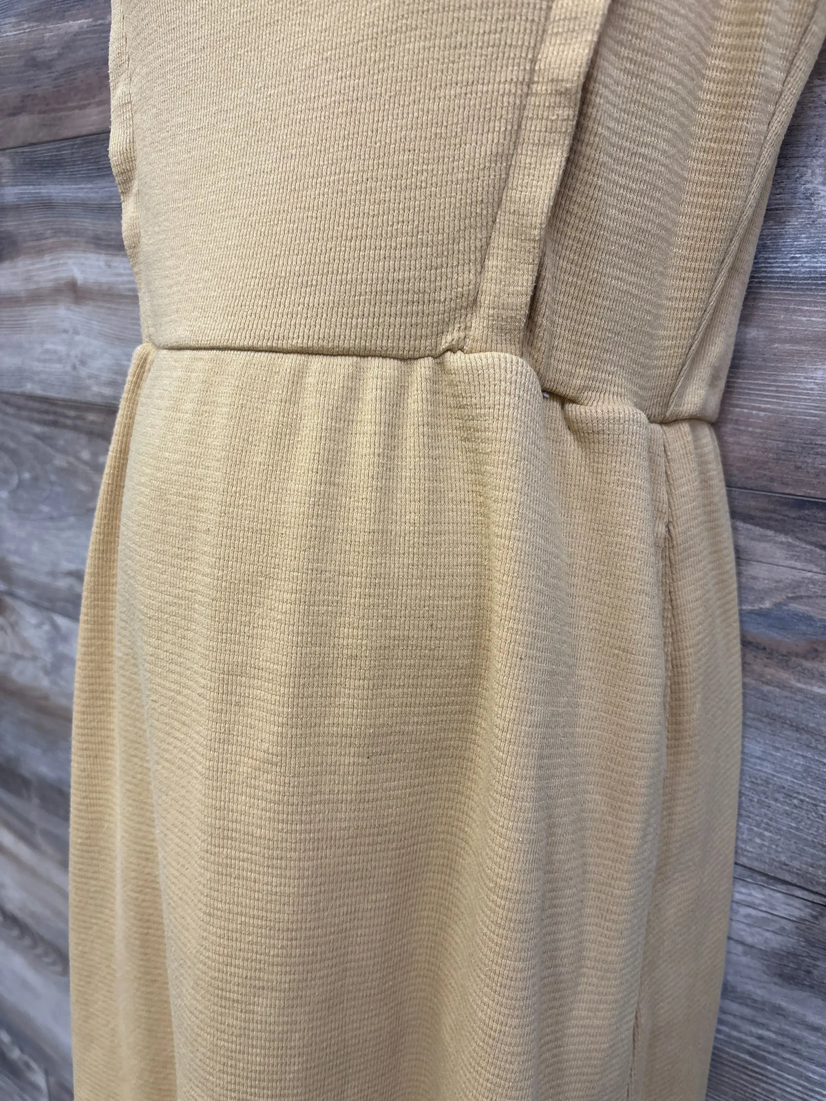 Side close-up of yellow Roolee maternity nursing tank dress showing waffle-knit texture and gathered waist seam against wood background