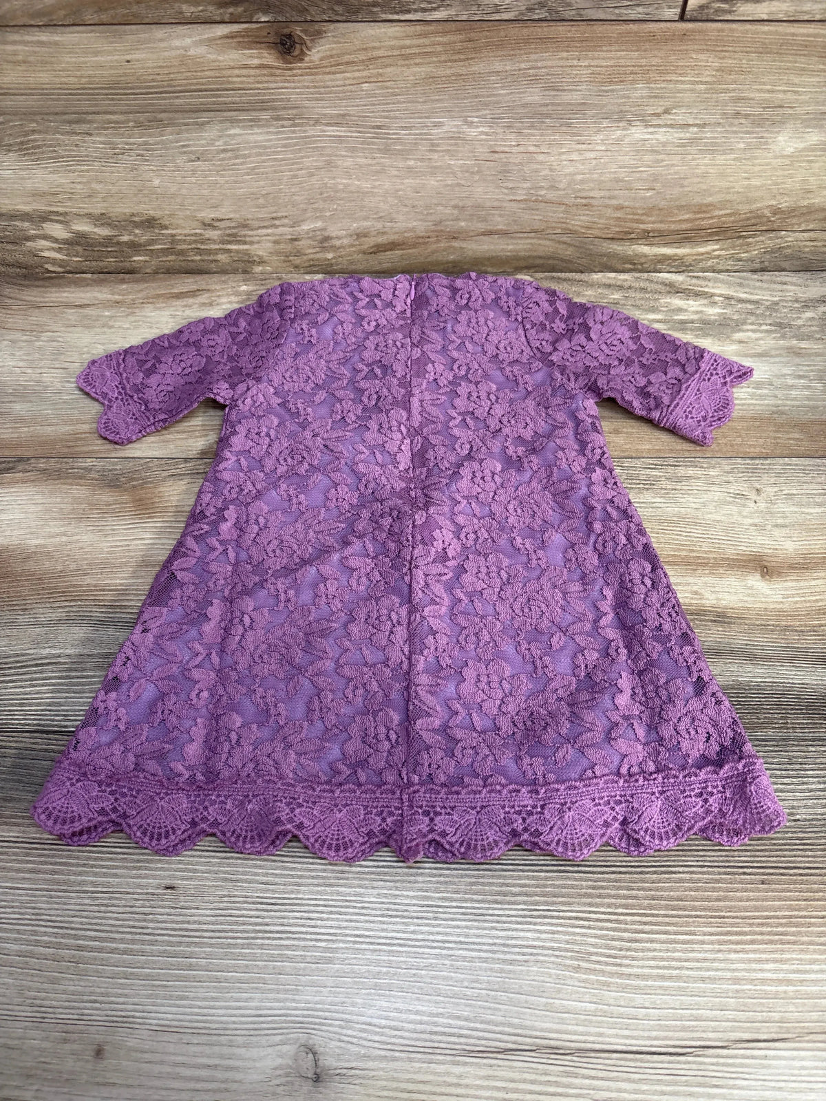 Flatlay back view of purple 3/4-sleeve baby dress showing floral lace overlay and scalloped hem on wood background