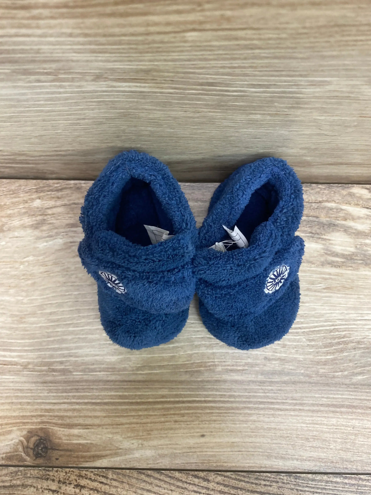 Top-down view of blue UGG Baby Bixbee baby boot pair showing plush shearling lining and embroidered logo on a wood surface