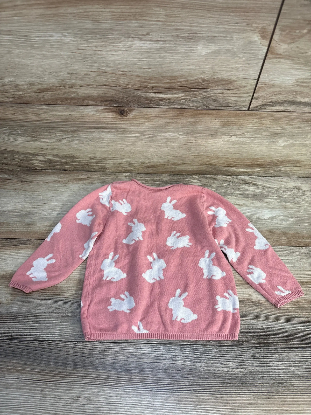 Pink kids sweater with white bunny print, long sleeves, laid on wood floor
