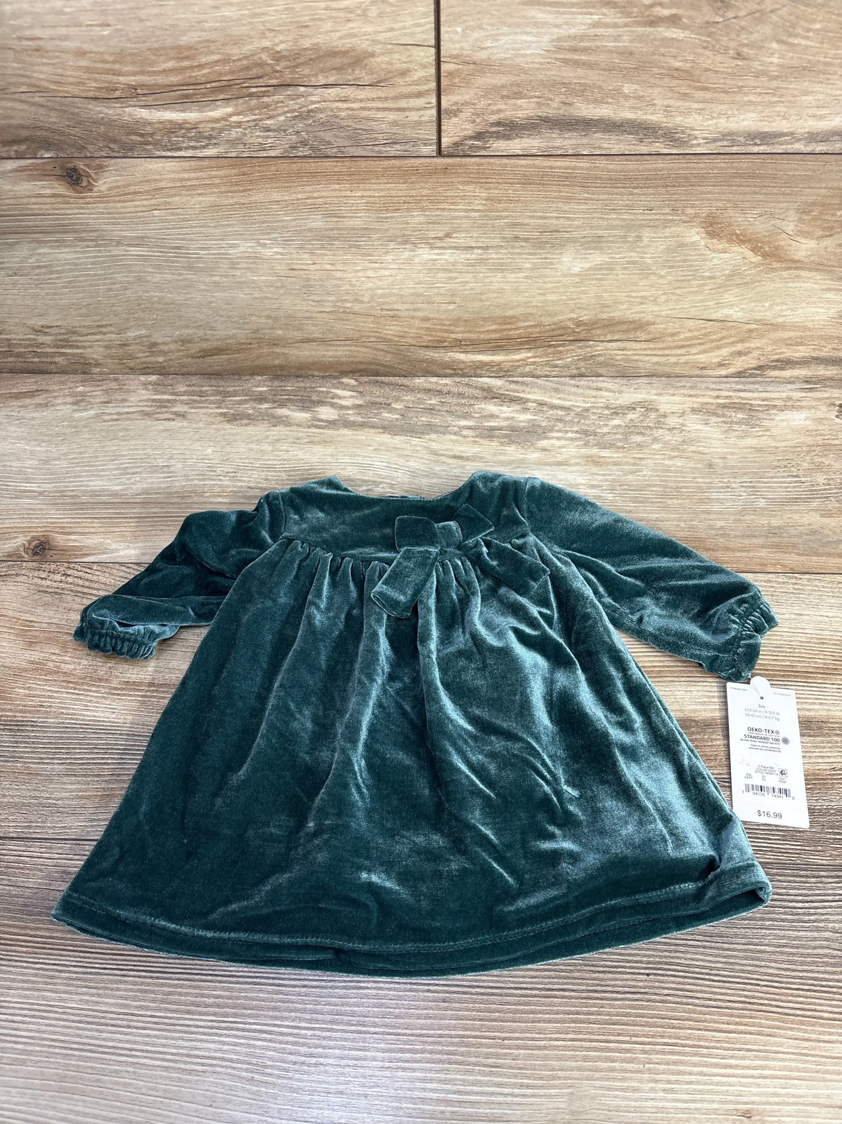 Flat lay of green Just One You velvet long sleeve bodysuit dress showcasing bow waist and long sleeves on wood plank floor
