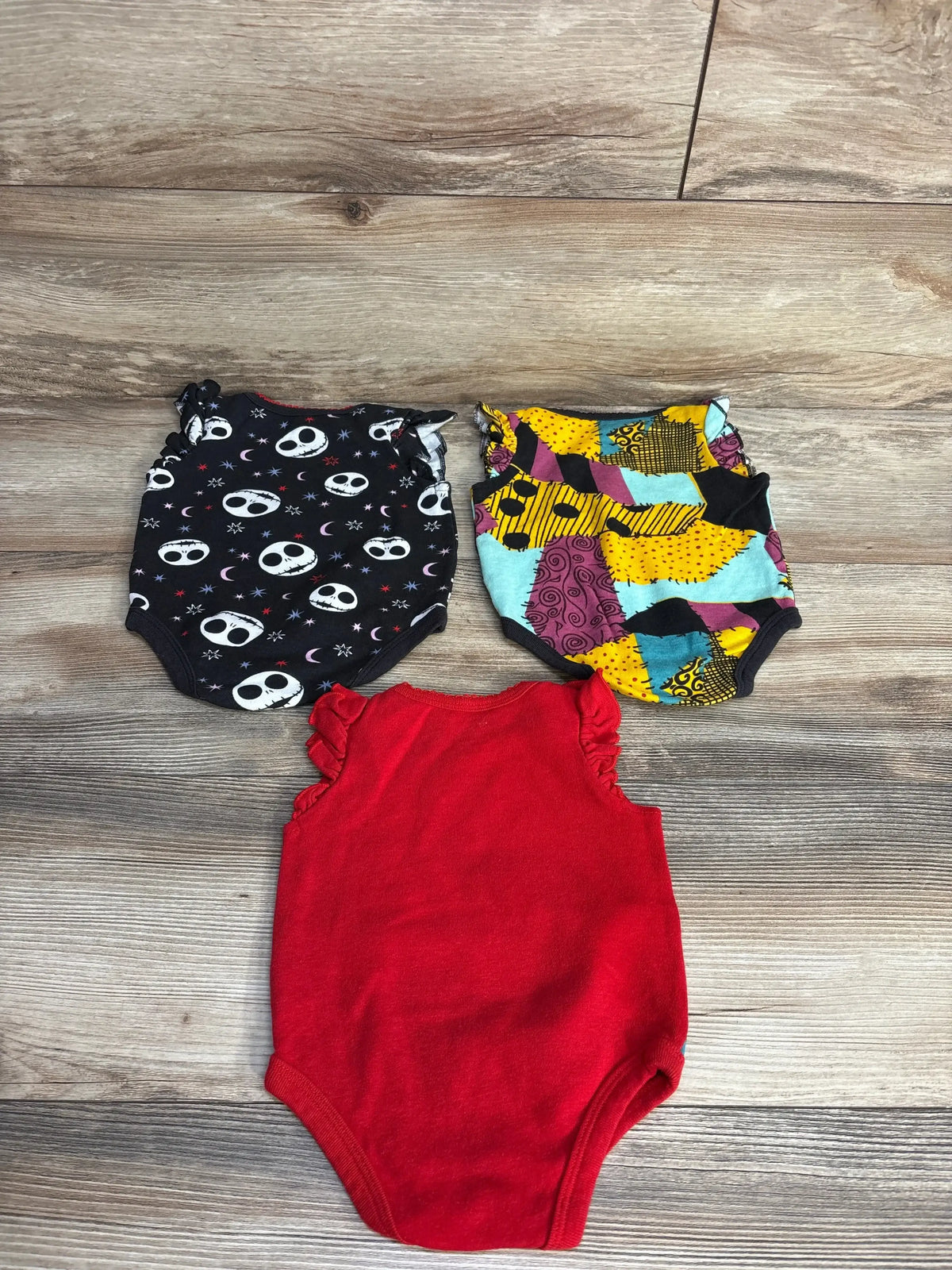 Top view of three Disney The Nightmare Before Christmas bodysuits, size 0-3m, with Skellington prints and red ruffles