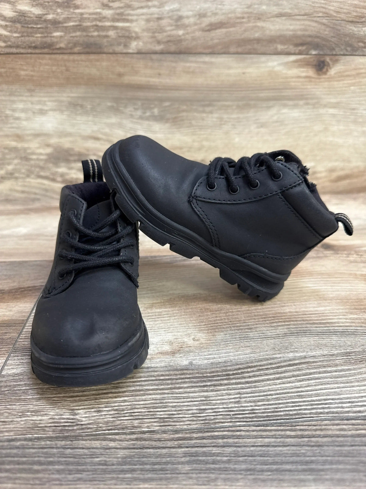 Front three-quarter of black Zara side-zip boots size 7C showing side zipper, laces and tread sole on wood background